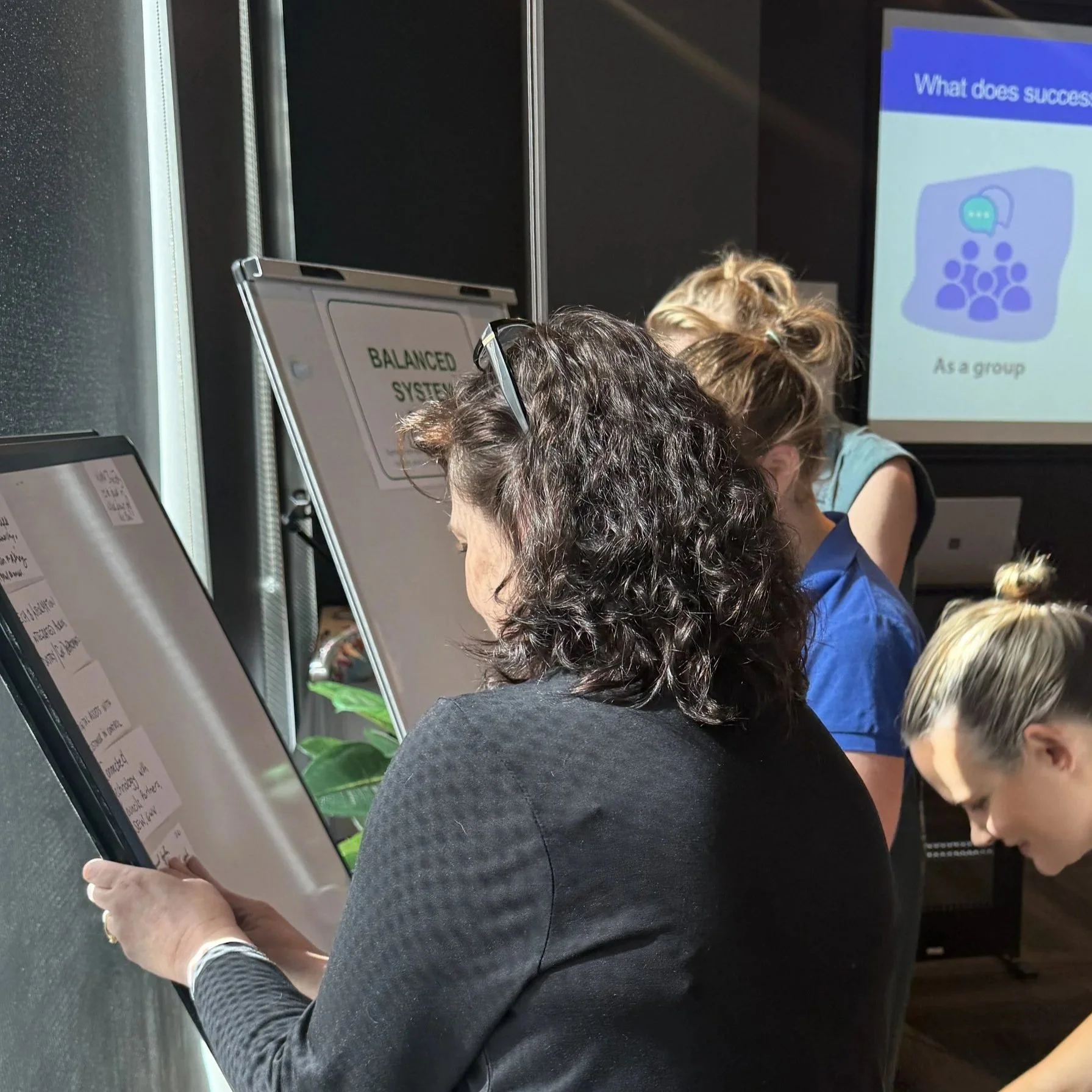 One person in a collaborative workshop working on a flipchart sorting different idea cards into key themes while others do the same nearby in the background.