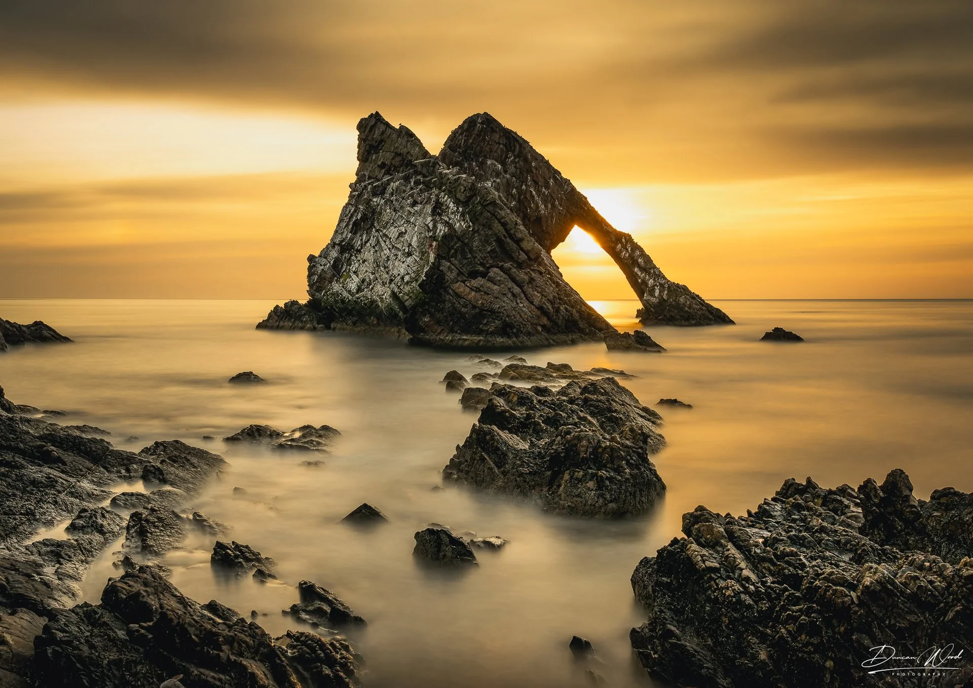 Bow Fiddle Rock sea arch at golden sunset, Portknockie, Scotland, long exposure photography by Duncan Wood.