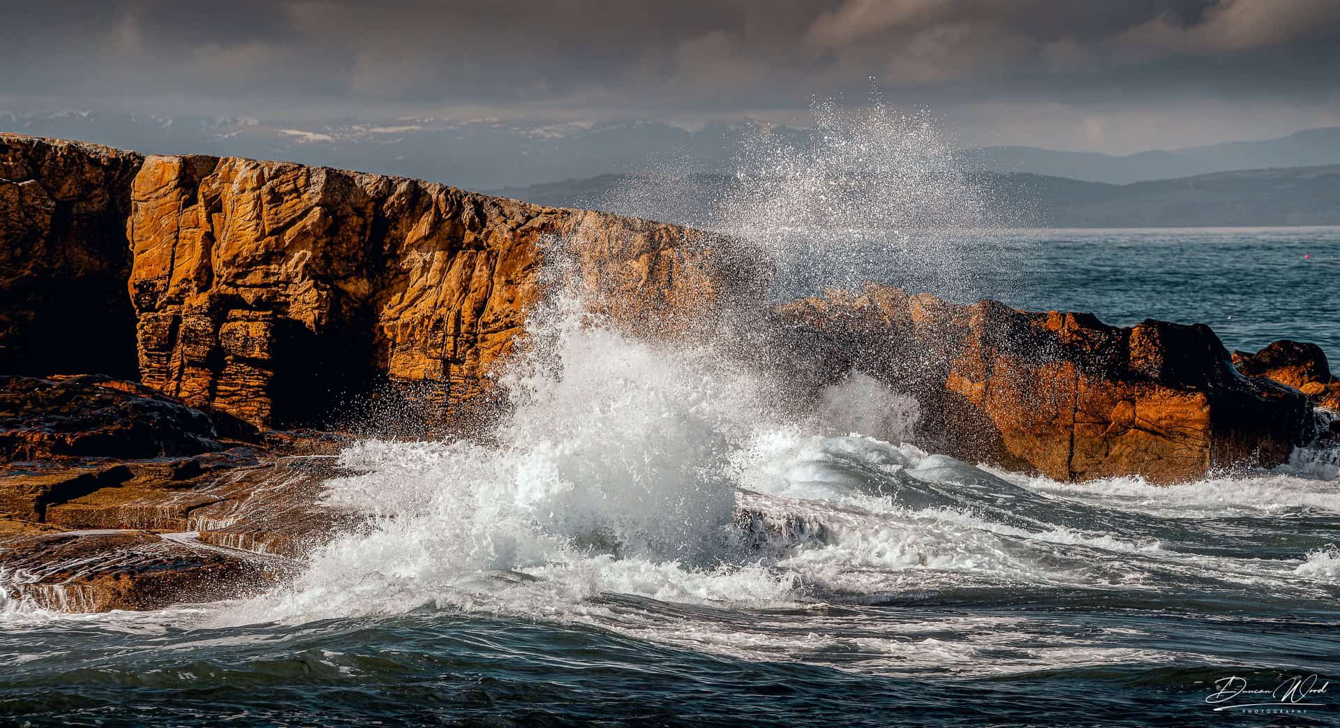 Waves breaking against red sandstone cliffs on Scotland’s east coast, representing intermediate coastal photography around Arbroath Cliffs.