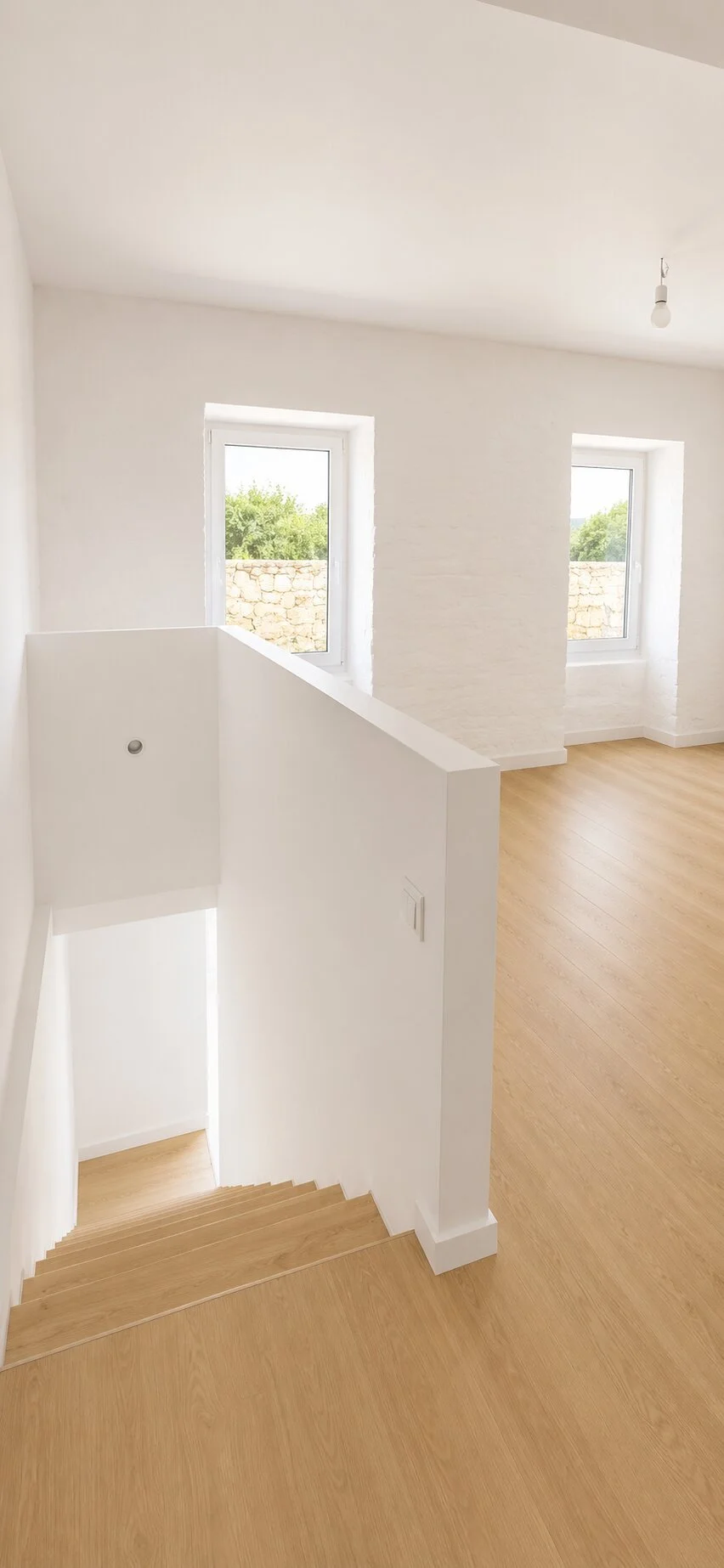 Renovated upper-floor room with exposed textured wall, white finishes and oak flooring