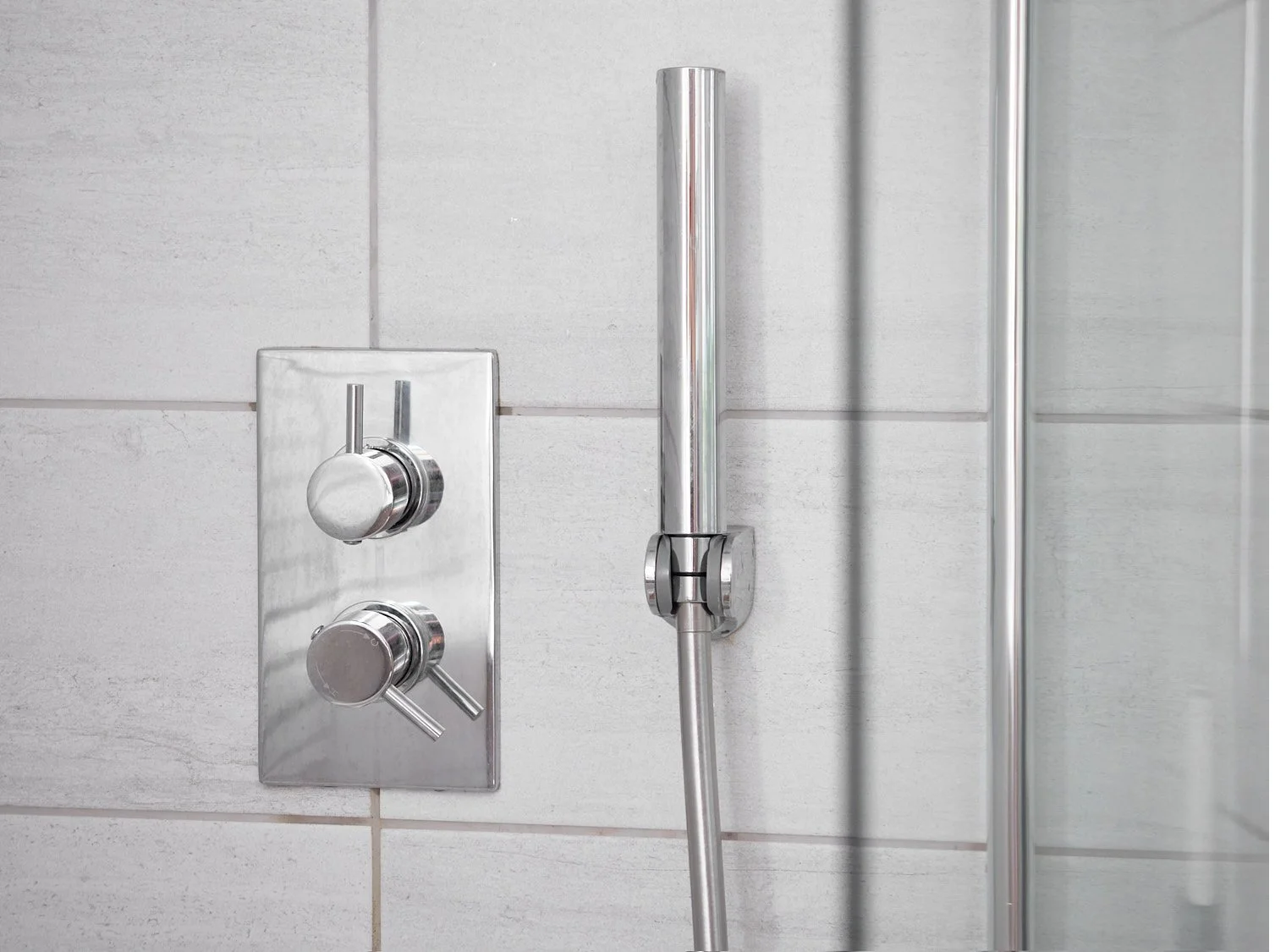hand held shower and shower controls against large grey bathroom tiles