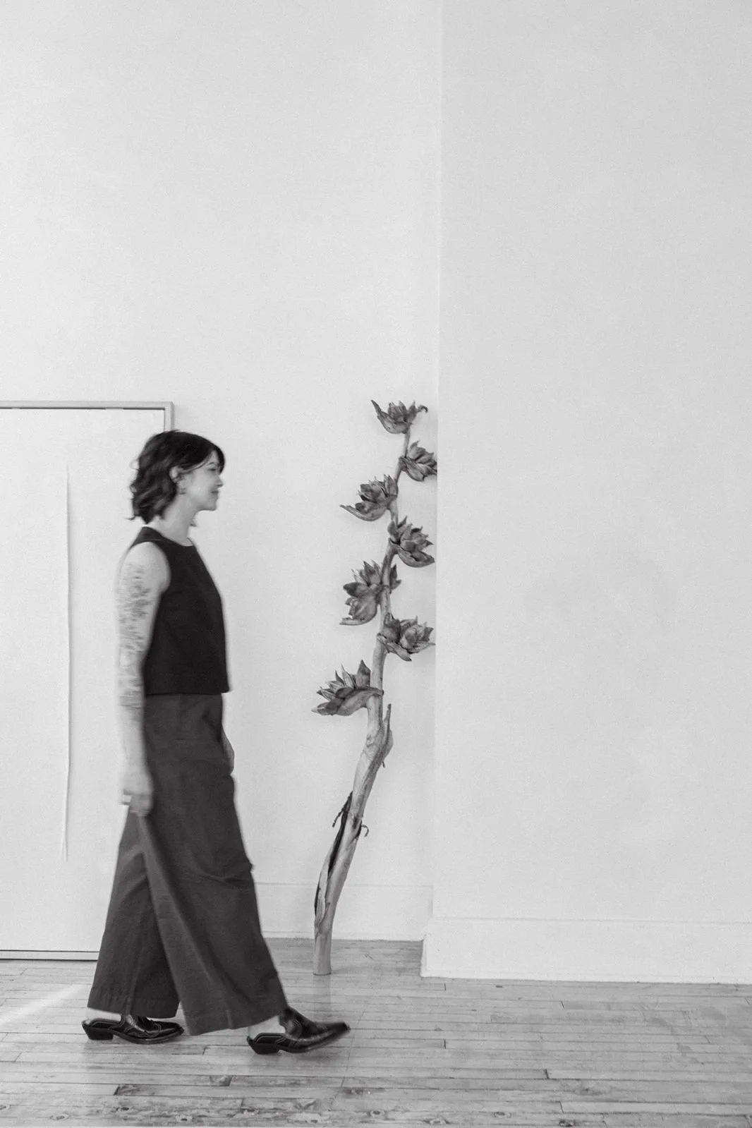 A woman walks past a wall with a vertical art installation of a branch with leaves and flowers.