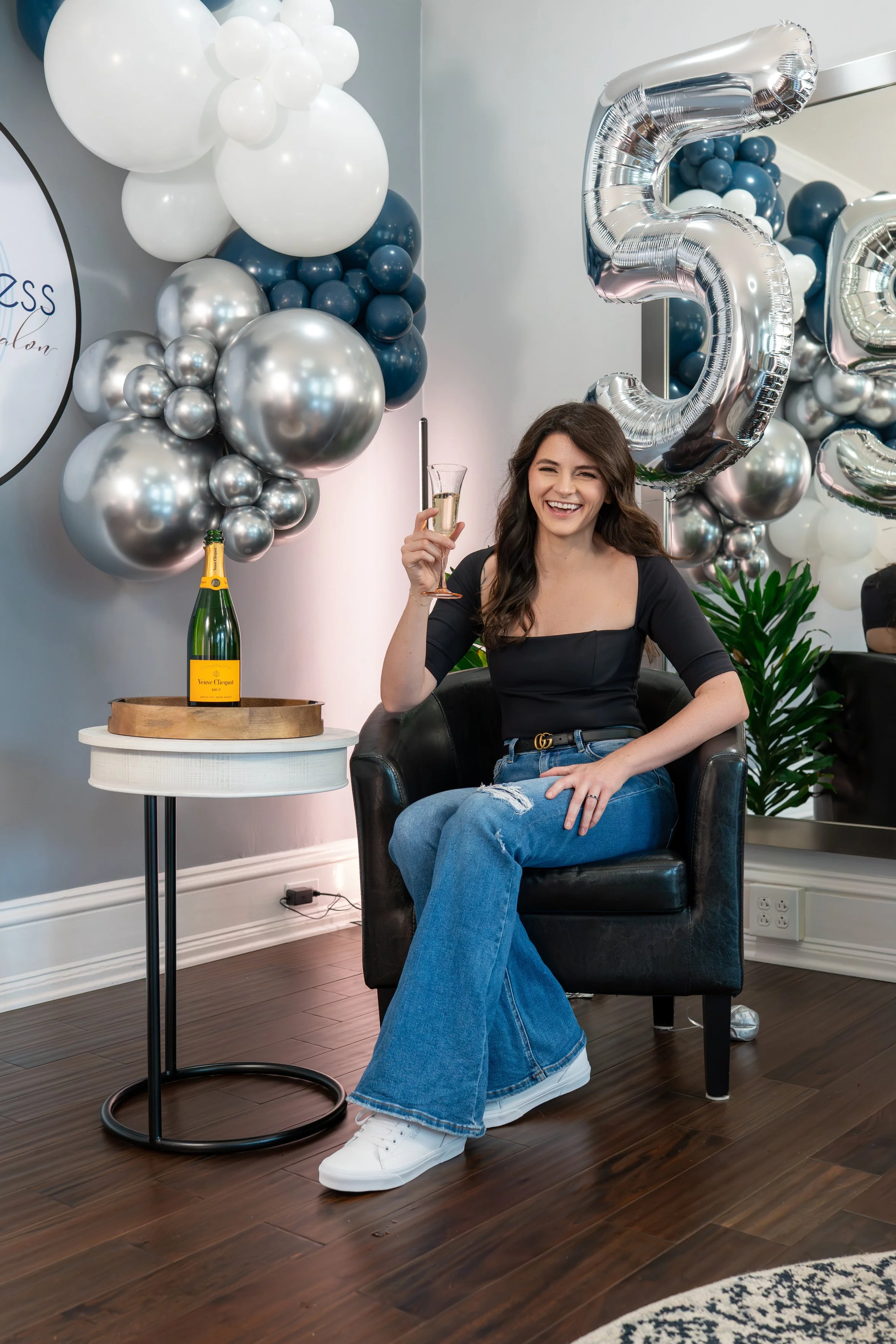 A woman sitting in a black chair holding a glass of champagne, celebrating 5 years in business
