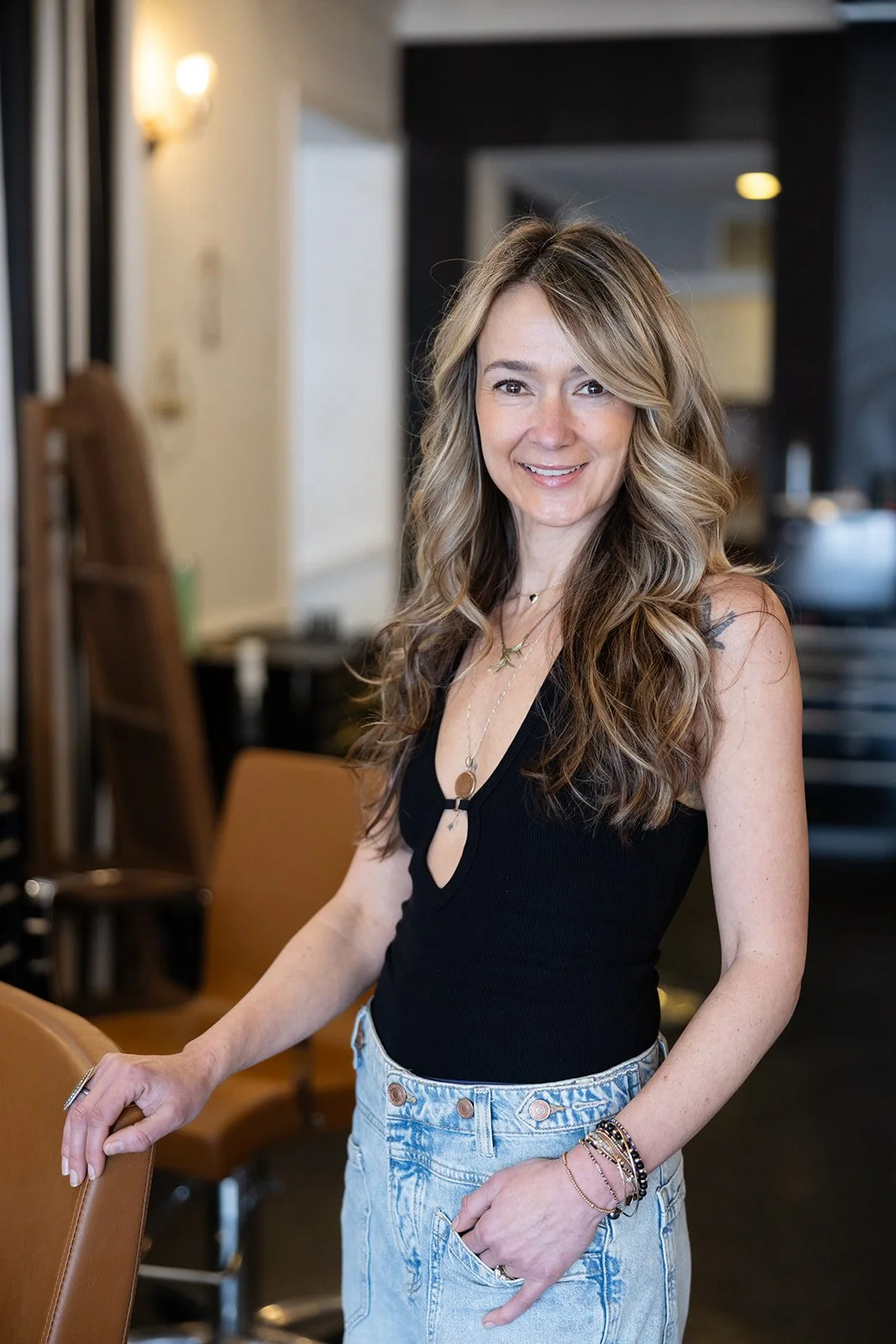 A smiling woman with wavy, shoulder-length red hair wearing a sleeveless white dress with pink and black geometric patterns.