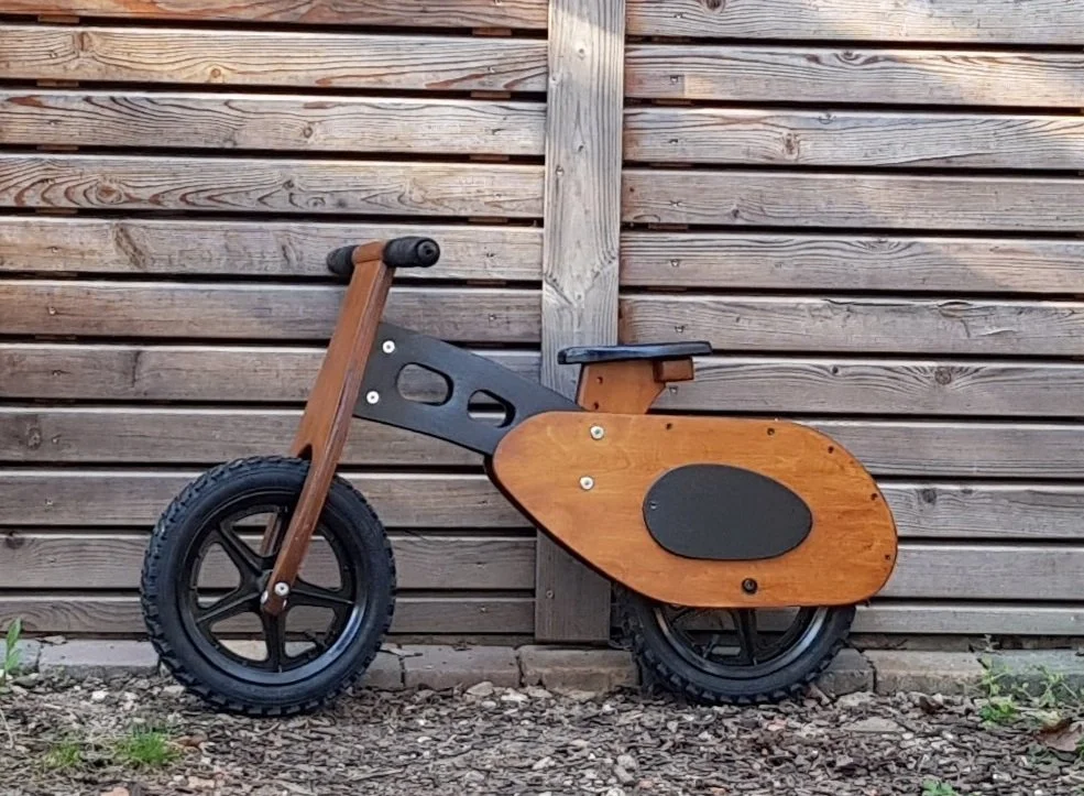Ein Holzspielzeug-Motorrad vor einem Holzzaun.