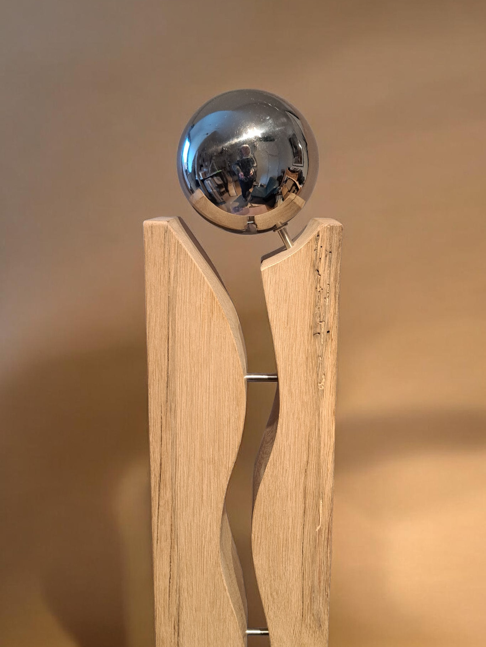 Ein modernes Kunstobjekt bestehend aus einem gebogenen Holzbalken mit einer metallischen Kugel auf einem kleinen Metallhalter.