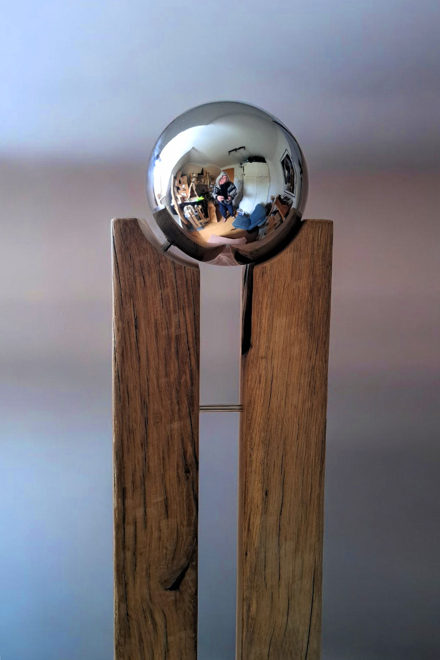 Reflexion eines Fotografen in einer silbernen Kugel, auf einem Holzgestell stehend.