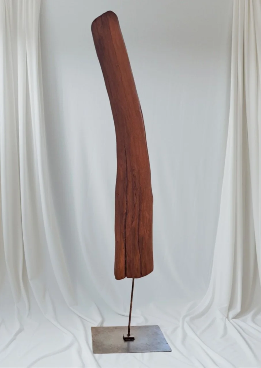 Ein aufrecht stehendes Kunstwerk aus Holz mit einer gebogenen Form, montiert auf einer metallenen Basis.