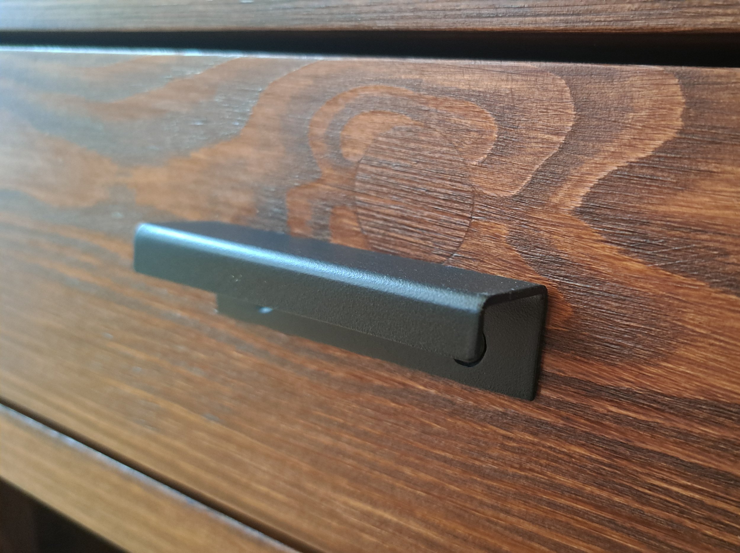 Nahaufnahme eines schwarzen Metallgriffs auf einer Holzoberfläche mit braunen Holzmaserungen.