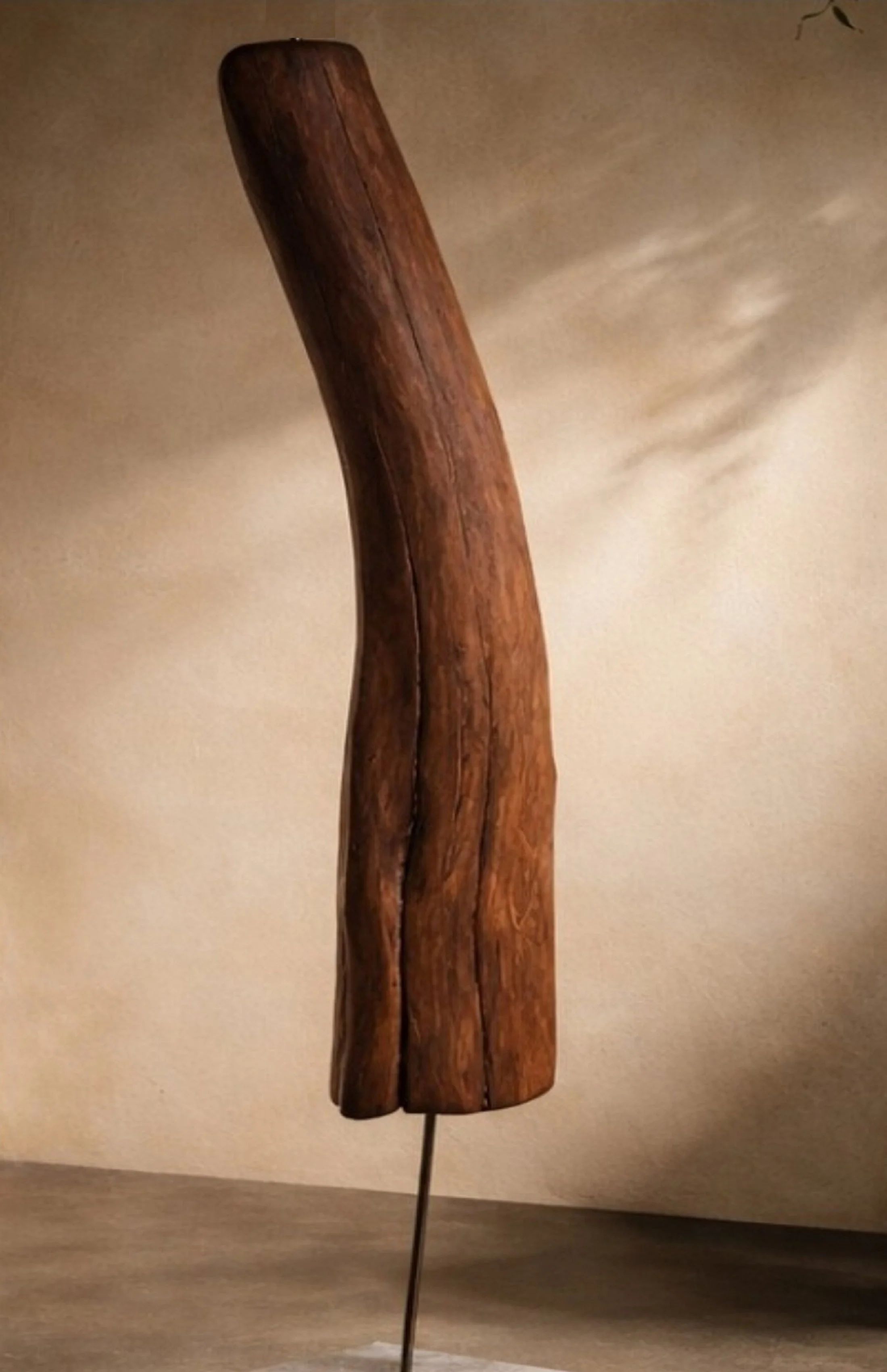 Ein kunstvoller, geschwungener Holzbalken auf einem Metallständer vor einer neutralen Wand.