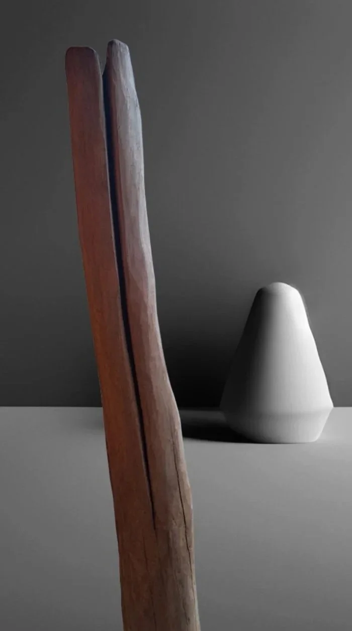 Abstrakte Stillleben mit zwei länglichen Holzstücken und einer weißen, kegelförmigen Skulptur auf einer grauen Oberfläche.
