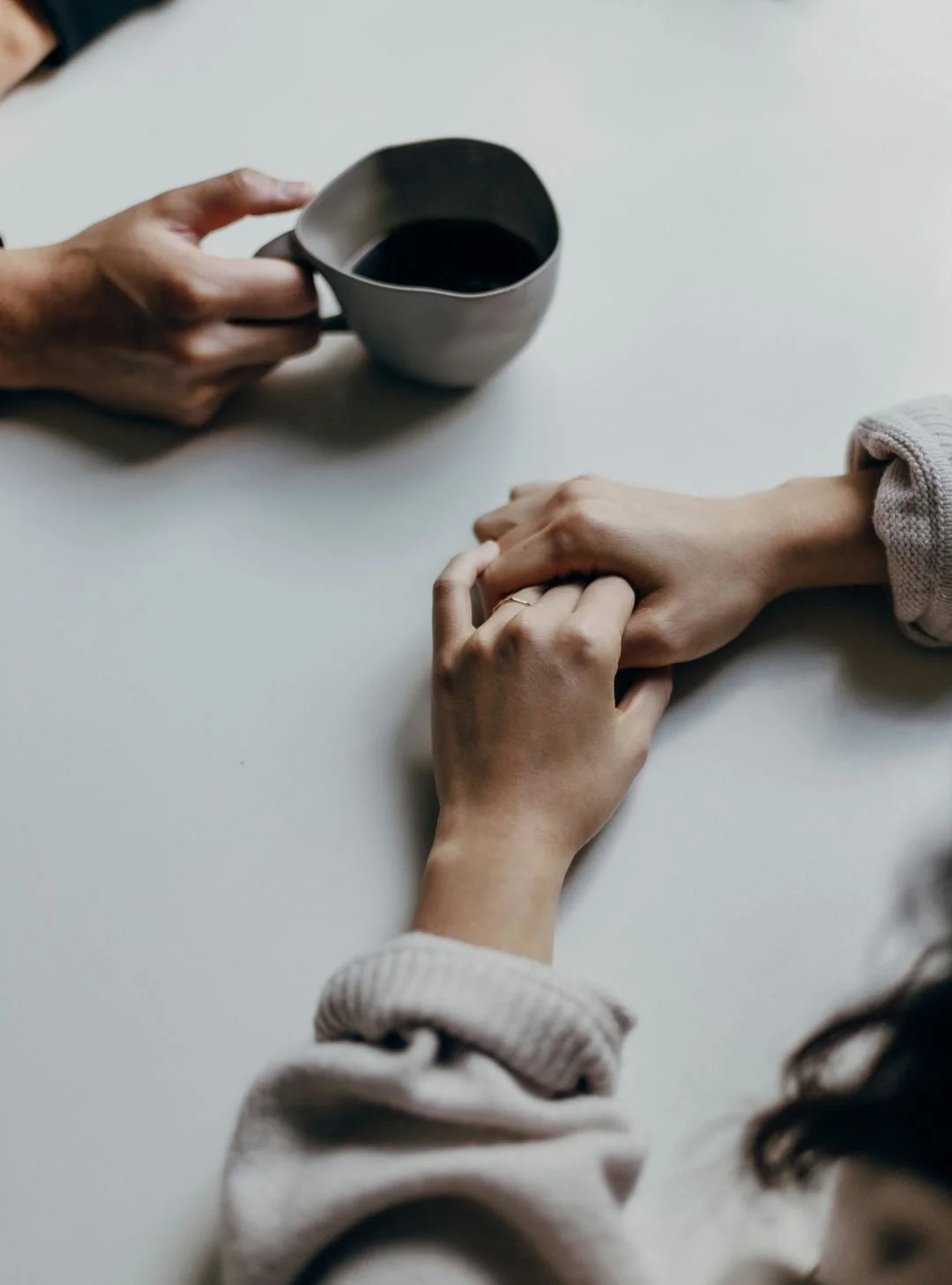 Two hands holding on a table, one person holding a coffee mug.