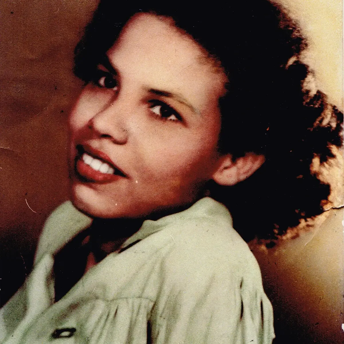 Portrait of a young Gloria Baylis looking toward the camera with a slight smile, wearing a light coloured blouse in a vintage photograph.