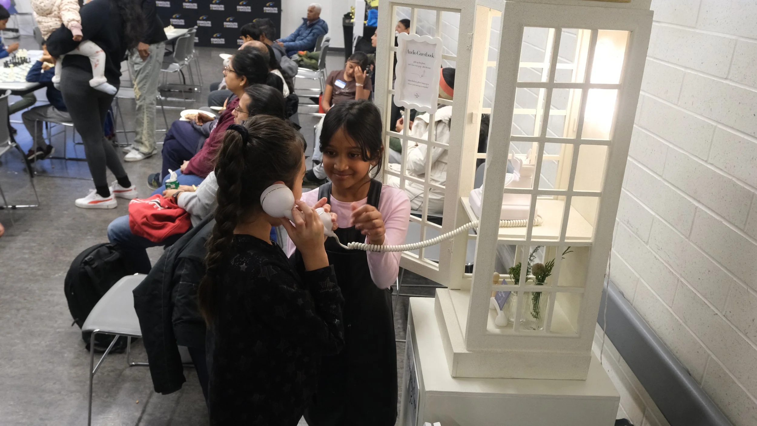 Two children using the interactive phone booth installation provided by The Keepsake Line at EnRoute 2 Success Chess Fest 2025.