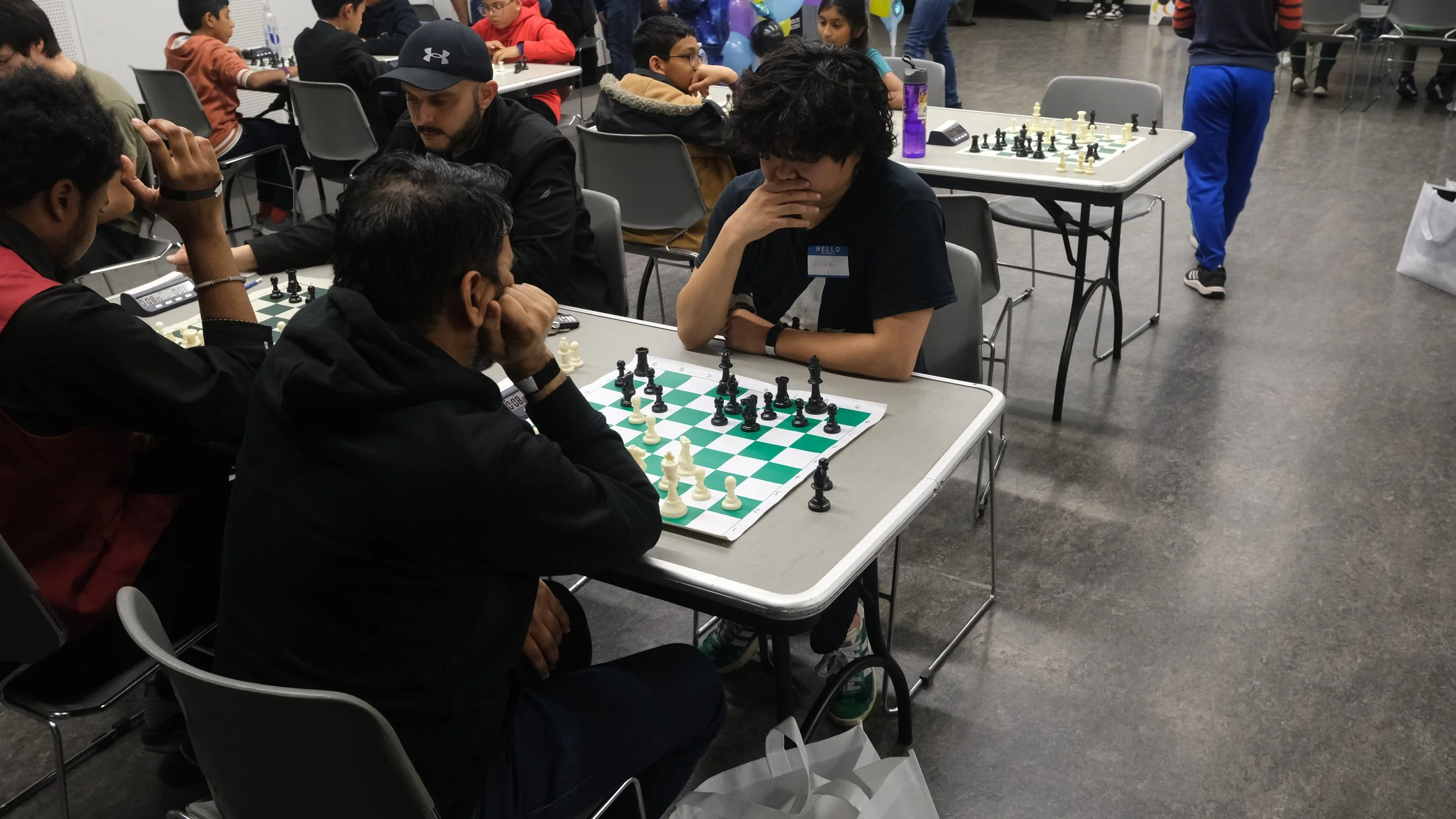 Players of different ages concentrate on chess matches at several tables during an EnRoute 2 Success chess tournament.