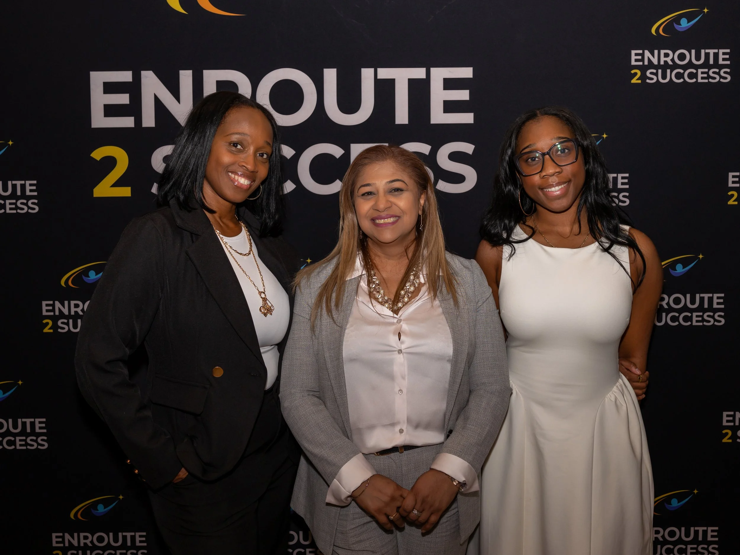 Three attendees posing in front of EnRoute 2 Success backdrop at Breaking Barriers: The Story of Gloria Baylis event