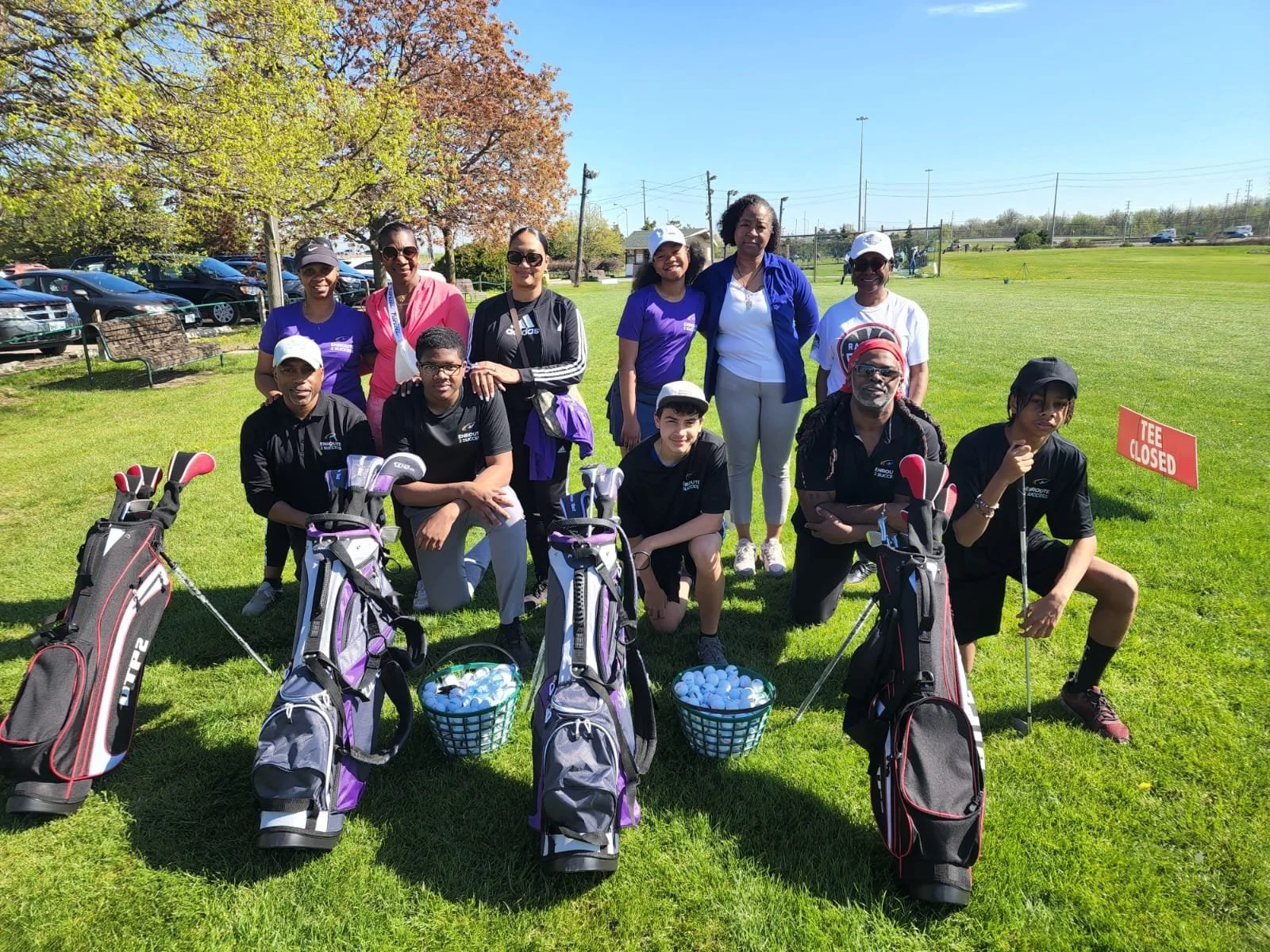Participants and coaches posing with golf equipment during an EnRoute 2 Success youth golf program