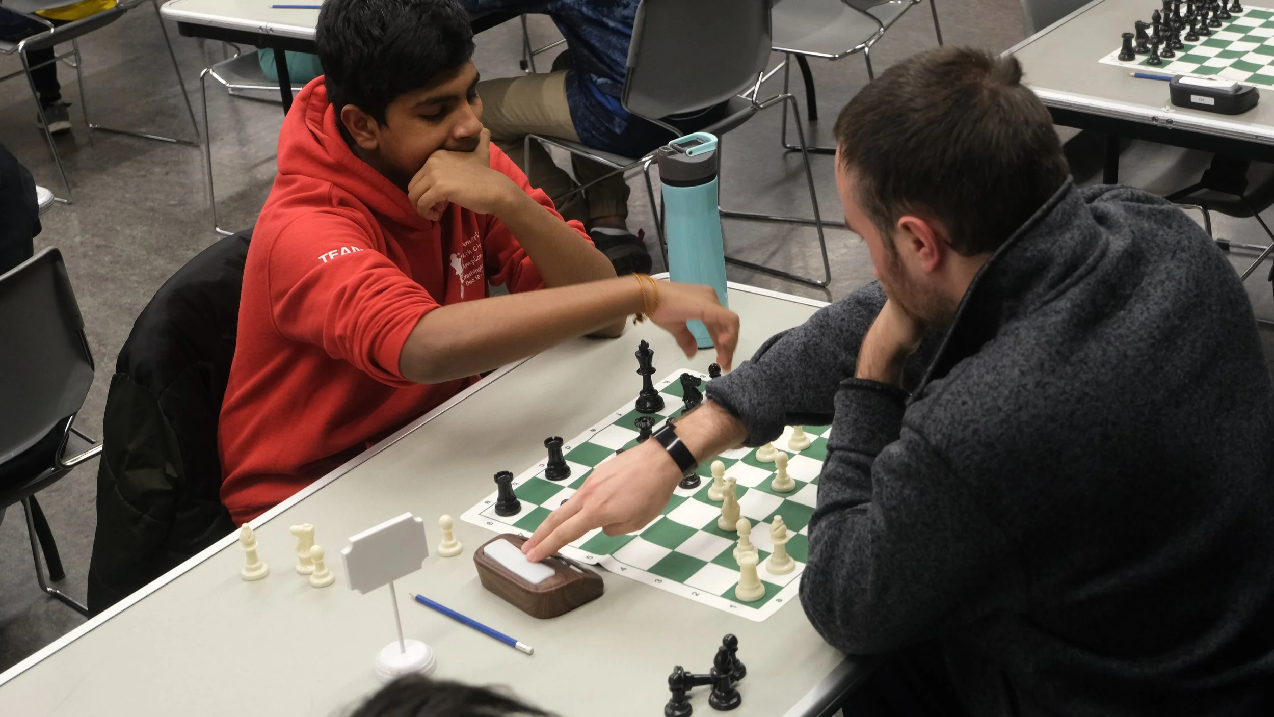 two players concentrate on chess matches at several tables during an EnRoute 2 Success chess tournament.