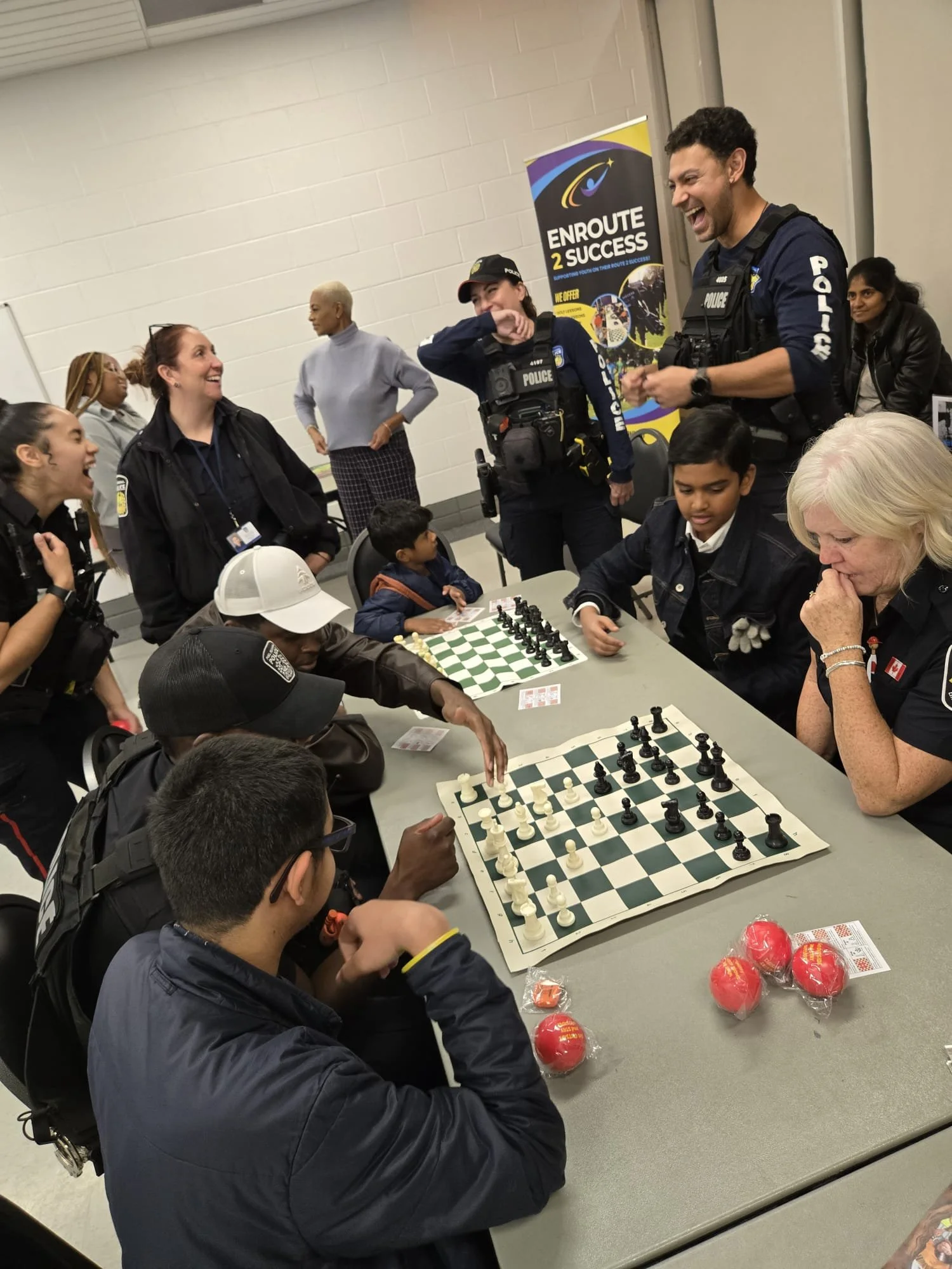 Youth playing chess with community members and police officers at an EnRoute 2 Success event