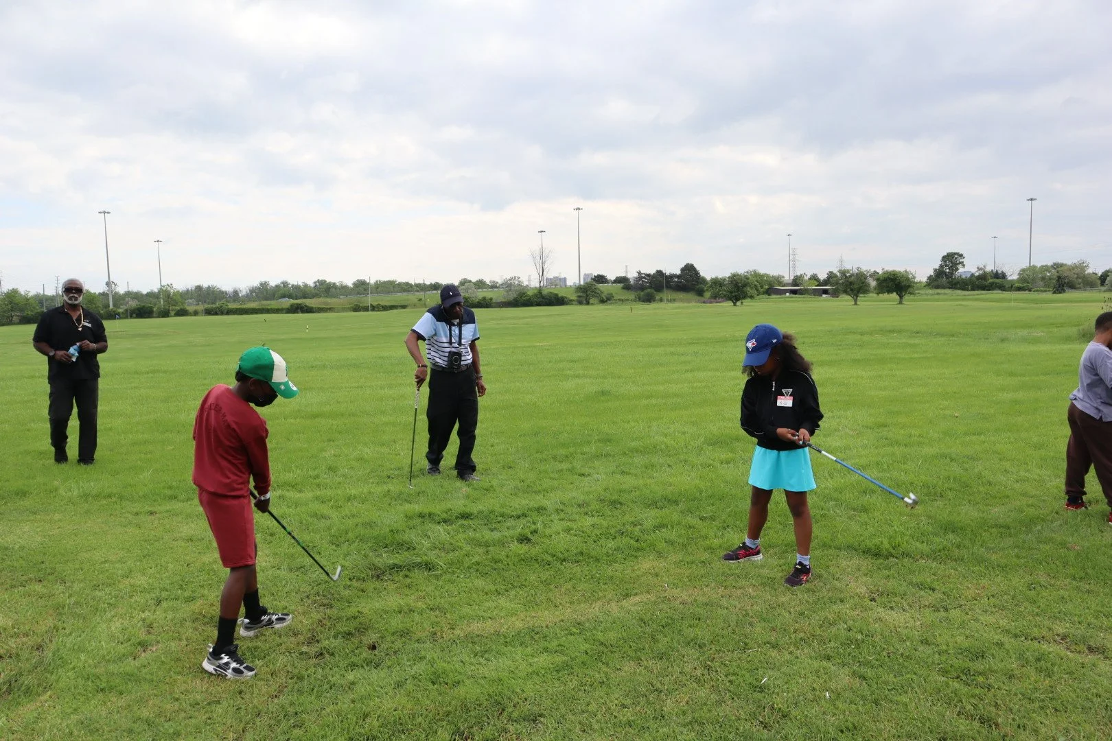 Two young golfers practicing their swings while instructors provide guidance during an EnRoute 2 Success free youth golf lesson at an outdoor driving range.
