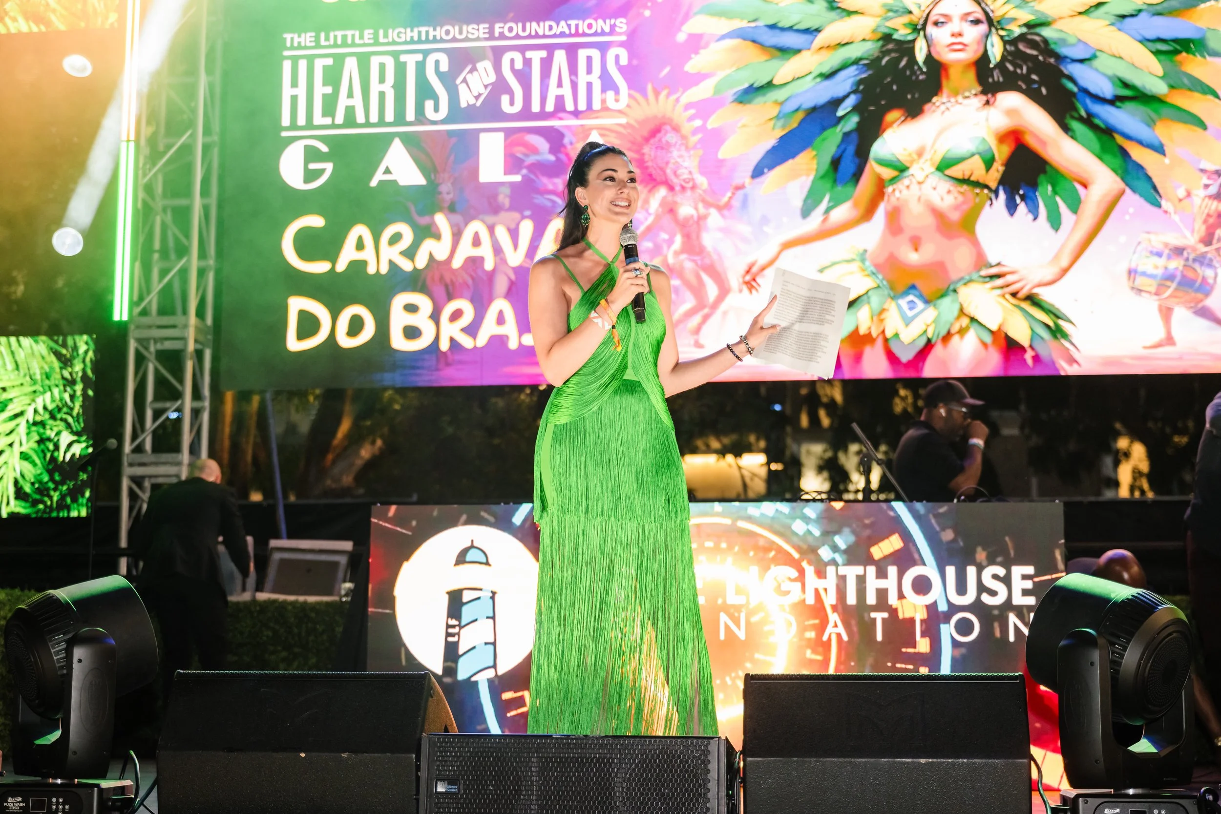 Speaker presenting on stage at the Little Lighthouse Foundation 2025 Hearts and Stars Gala Carnaval do Brasil theme at Jungle Plaza Miami Design District