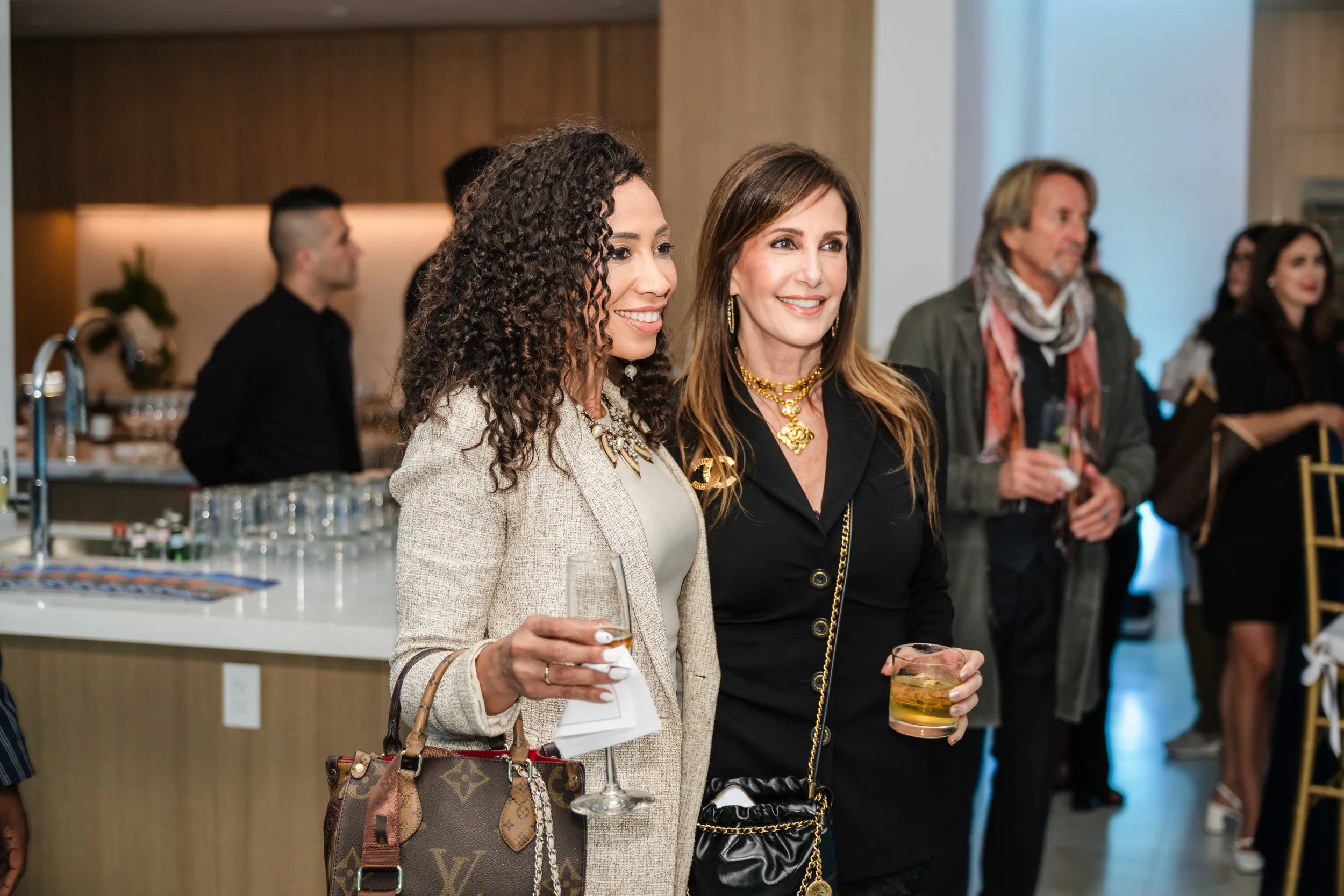 Two women posing with drinks near the bar at a luxury real estate event at Pier Sixty-Six Fort Lauderdale