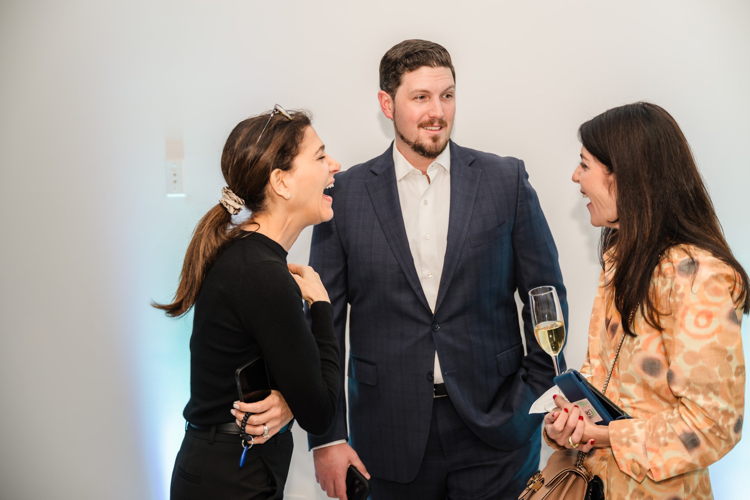 Three professionals laughing and networking with champagne at a real estate networking event at Pier Sixty-Six Fort Lauderdale