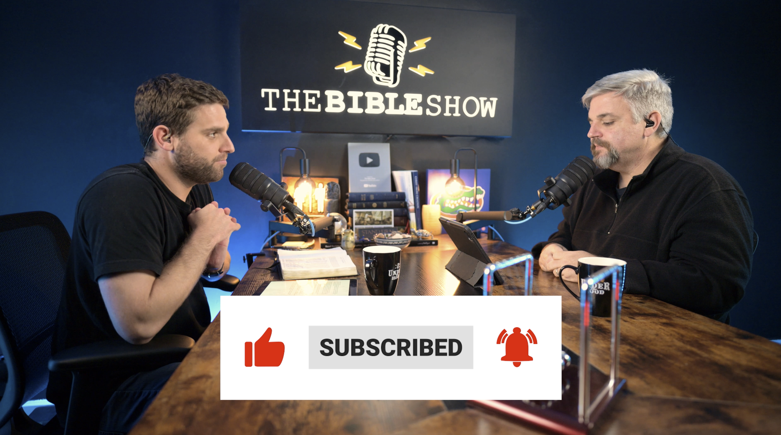 Two Bible Show hosts record a video podcast with an on-screen YouTube subscribe, like, and notification graphic.