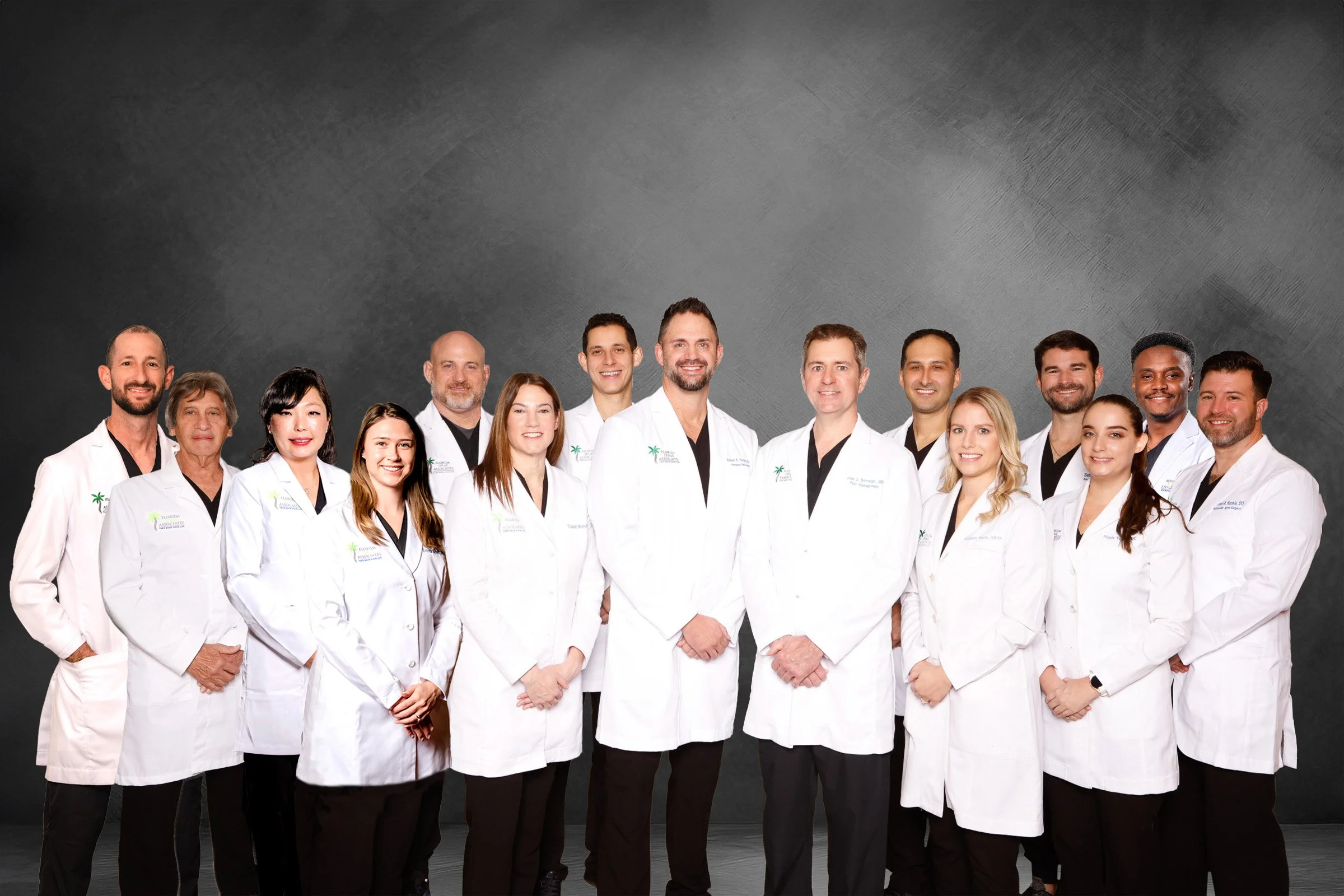 Group of healthcare professionals in white coats standing together against a dark grey background, smiling at the camera.