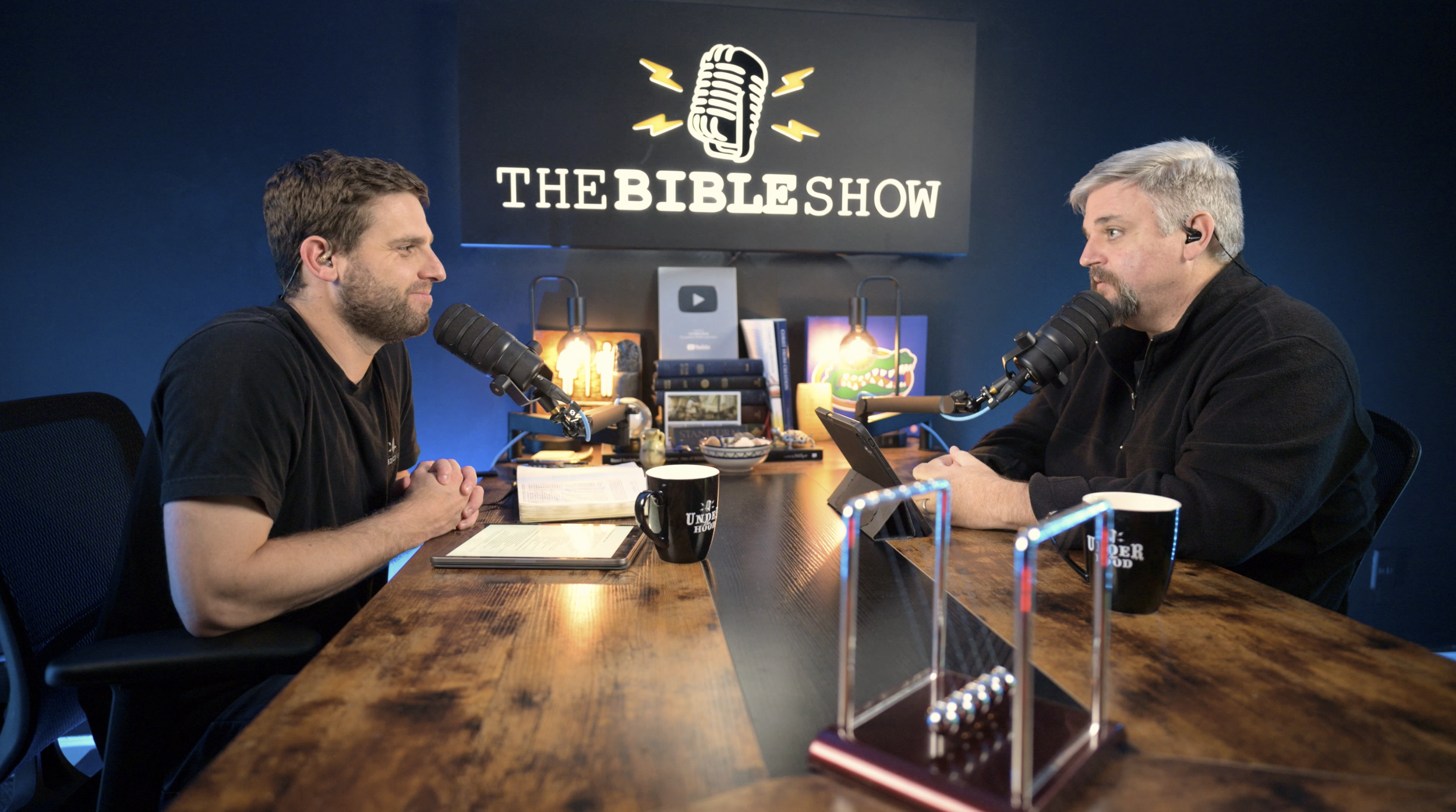 Two Bible Show hosts record a video podcast episode about the historical background of the Gospel of Matthew in a professional studio.