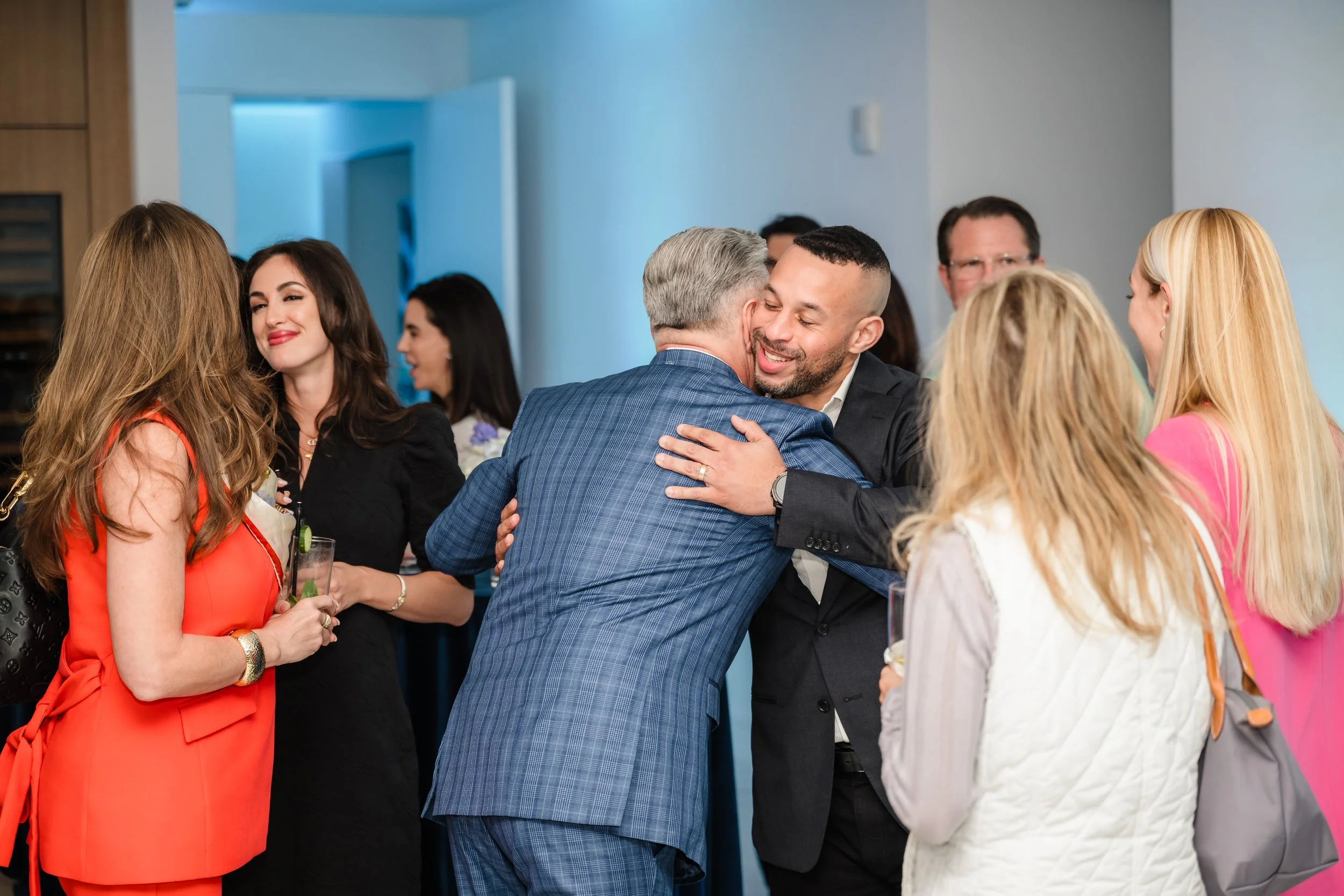 Two men embracing while guests network with cocktails at a real estate event at Pier Sixty-Six Fort Lauderdale