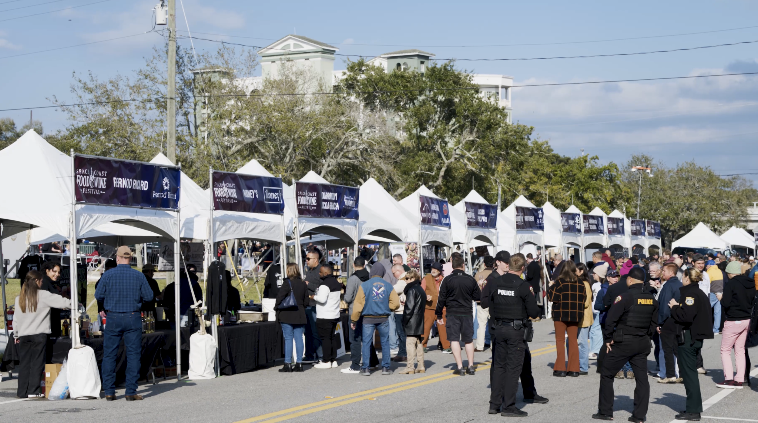 Crowds of festival-goers enjoying wine tastings and food samples in front of branded vendor tents including Boardroom Cocoa Beach at the Space Coast Food & Wine Festival in Melbourne, Florida