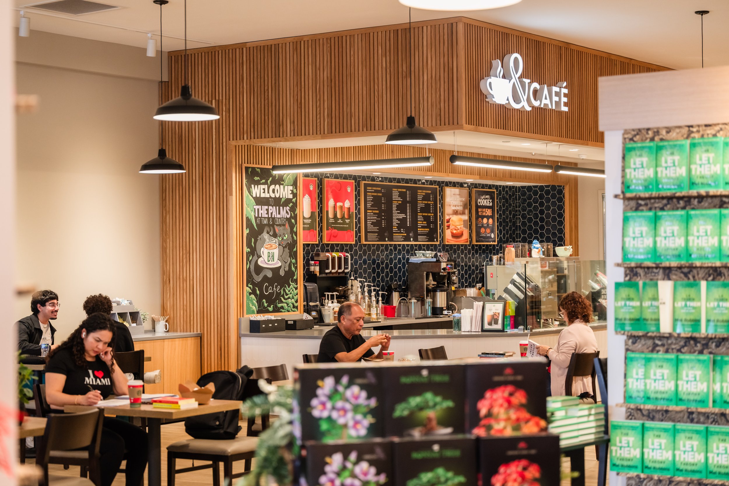 Inside a coffee shop with wooden paneling, customers sitting at tables, and a counter with a menu board. Customers are enjoying their drinks, and the shop has a cozy atmosphere.