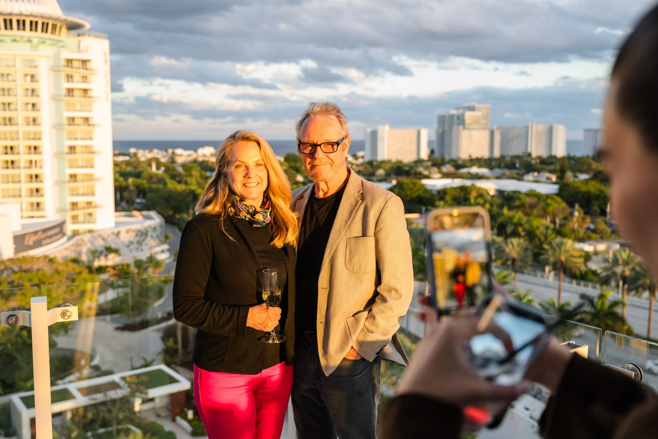 Couple posing with champagne on a balcony overlooking the Fort Lauderdale skyline at a real estate event at Pier Sixty-Six