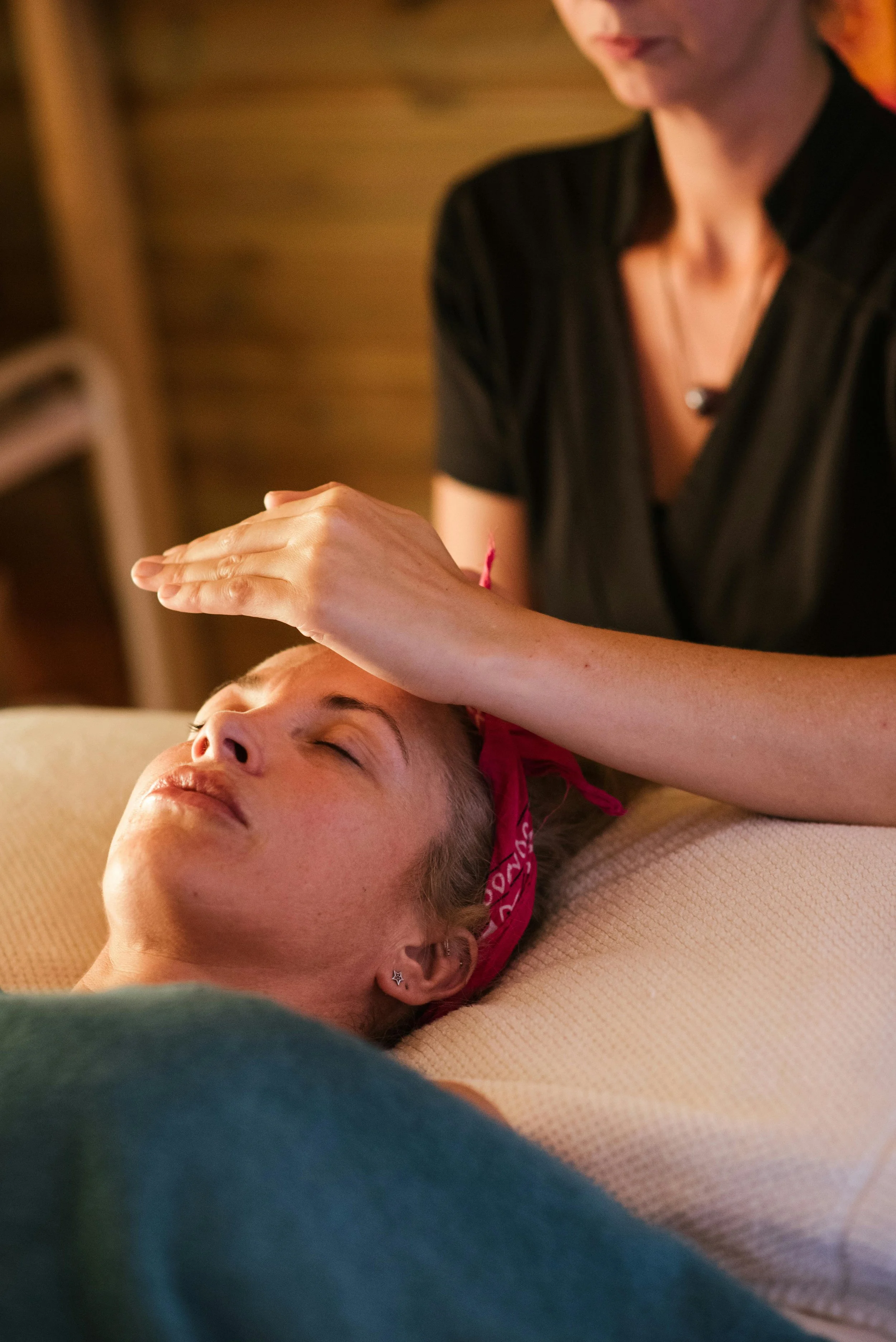 A woman receiving reiki from a therapist in a dimly lit room.