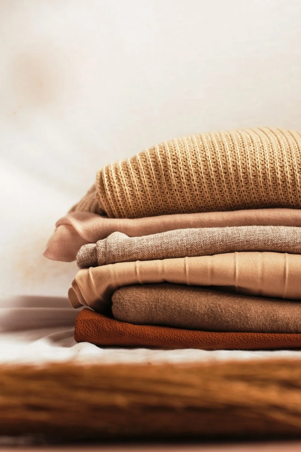 a stack of warm-toned knits, sweaters, and other clothing folded in a pile