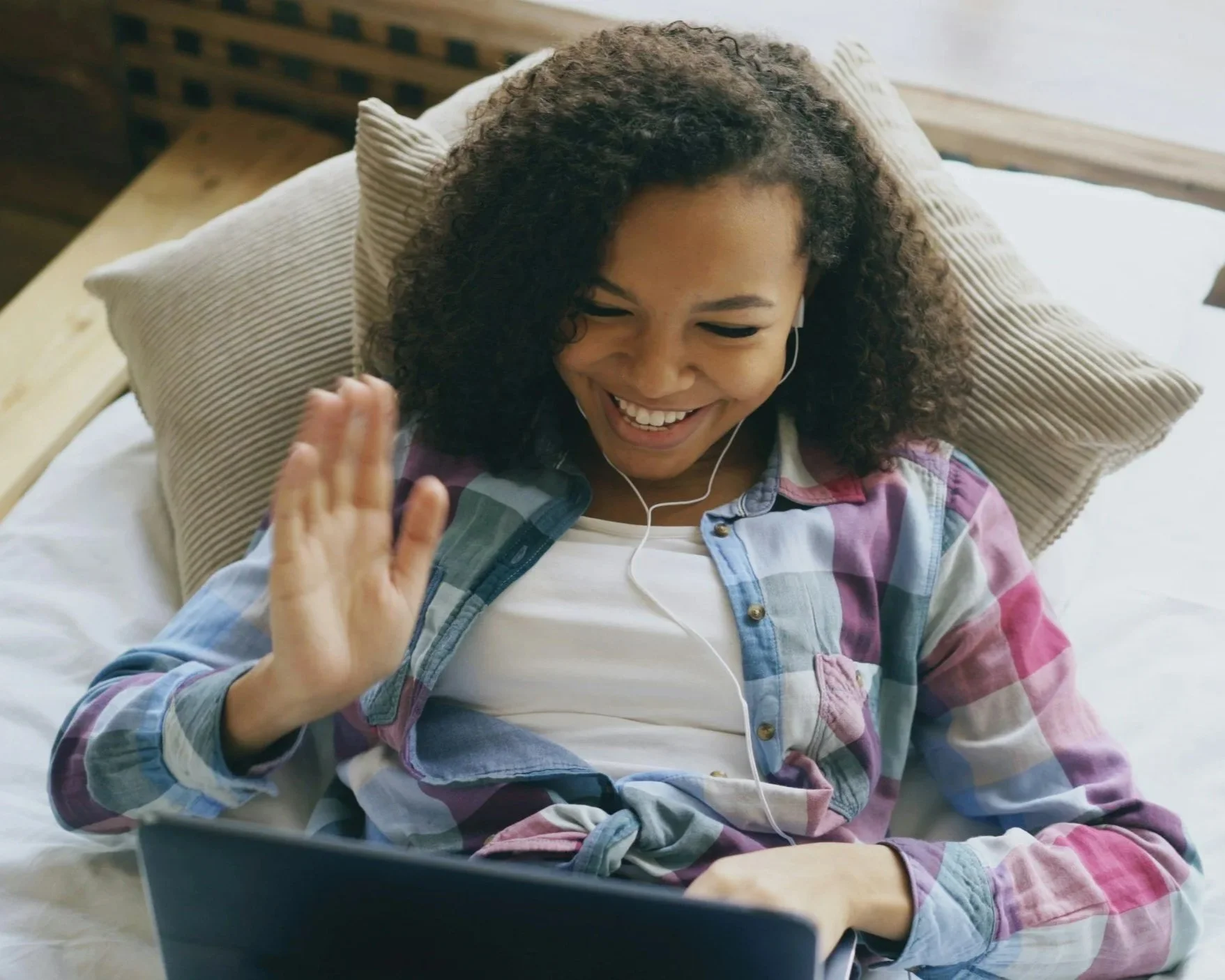 Woman smiling and waving during a video call on her laptop while wearing earbuds
