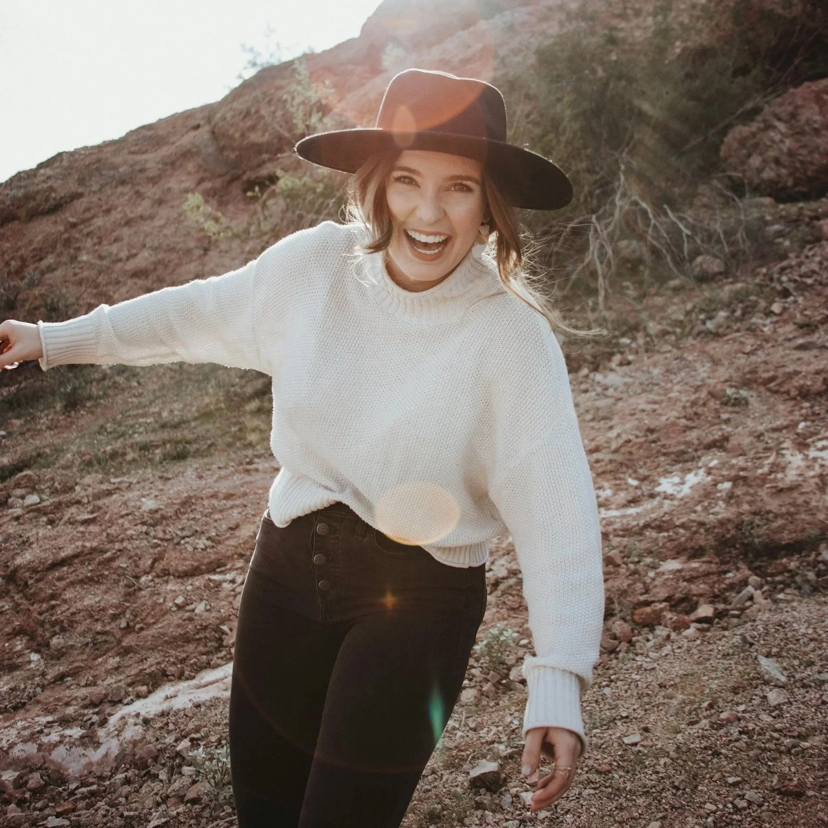 Woman laughing outdoors in a desert landscape with warm sunlight