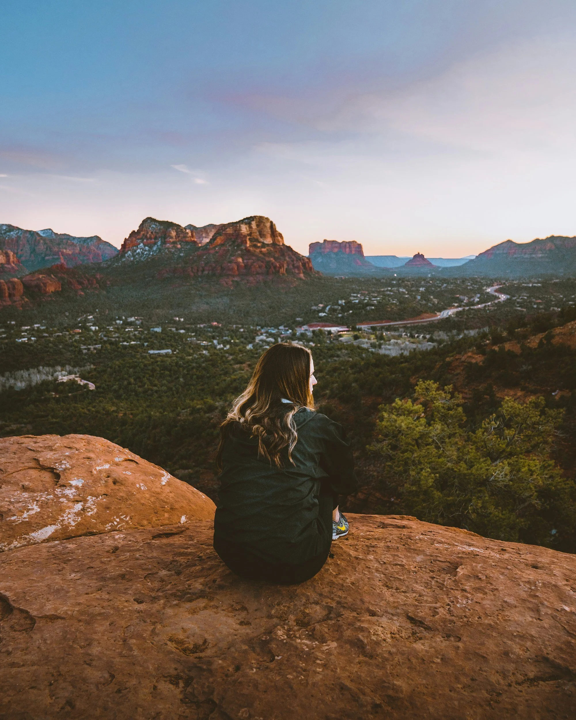 Woman sitting on a red rock overlook, looking out across a desert landscape and canyon scenery in Arizona