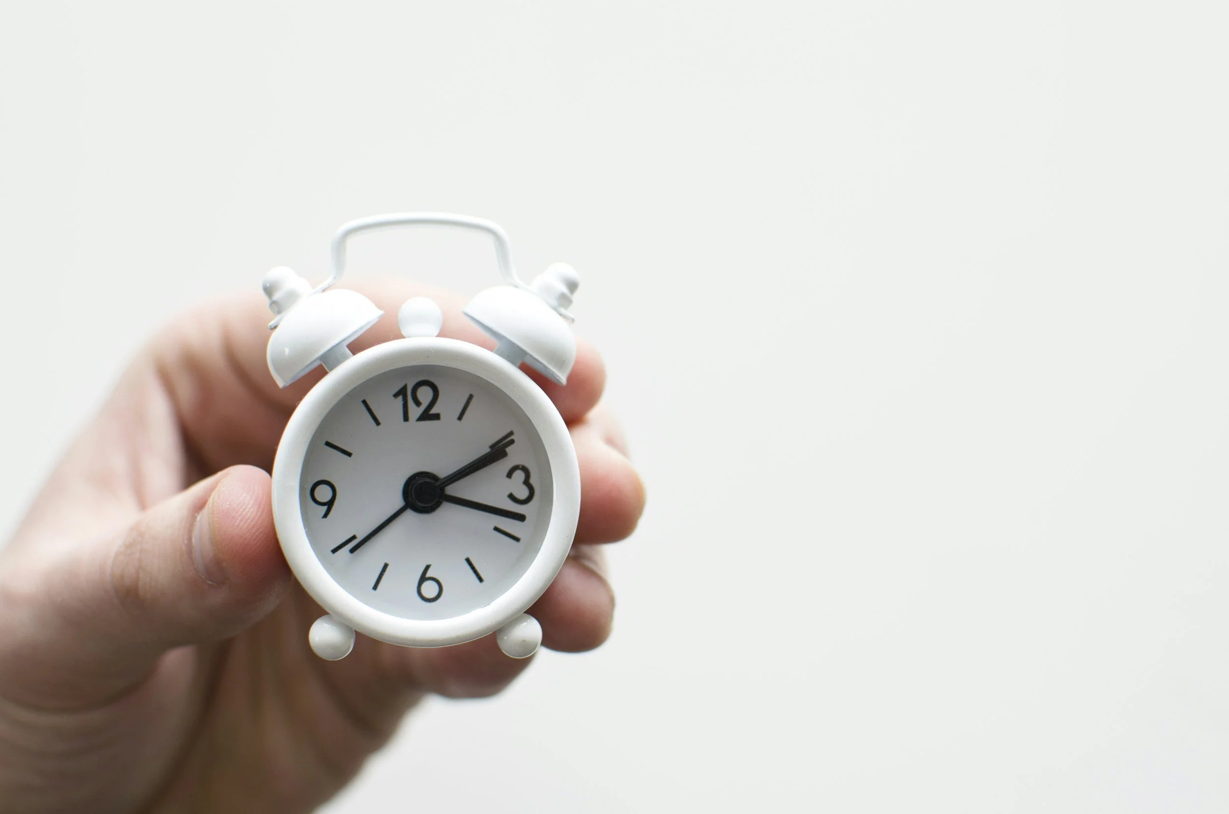 Hand holding a small alarm clock against a neutral background, representing dedicated time for focused healing and personal growth.