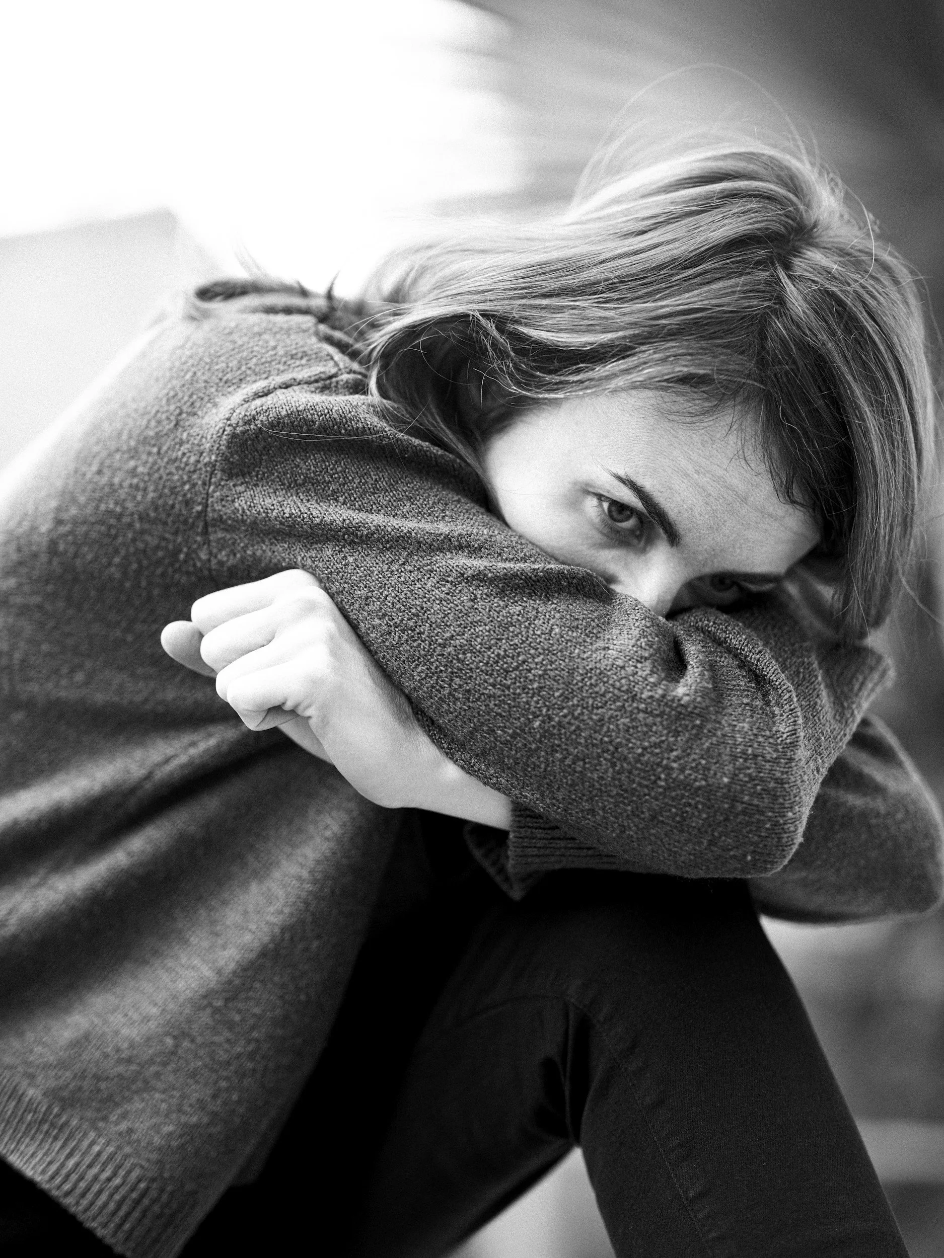 Black-and-white portrait of a person sitting with their arms wrapped around their knees.