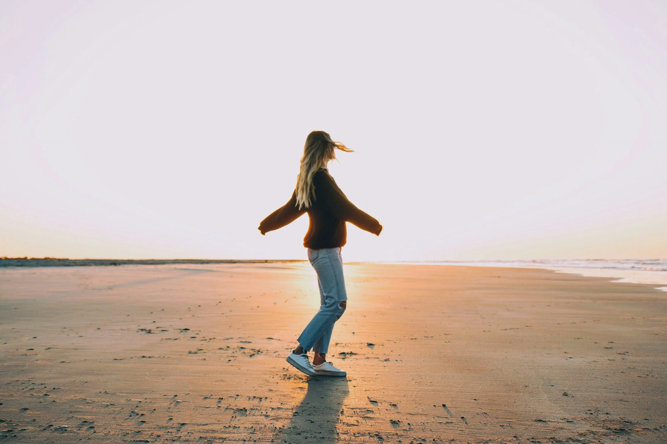 Woman walking along a beach at sunset with her hair blowing in the wind