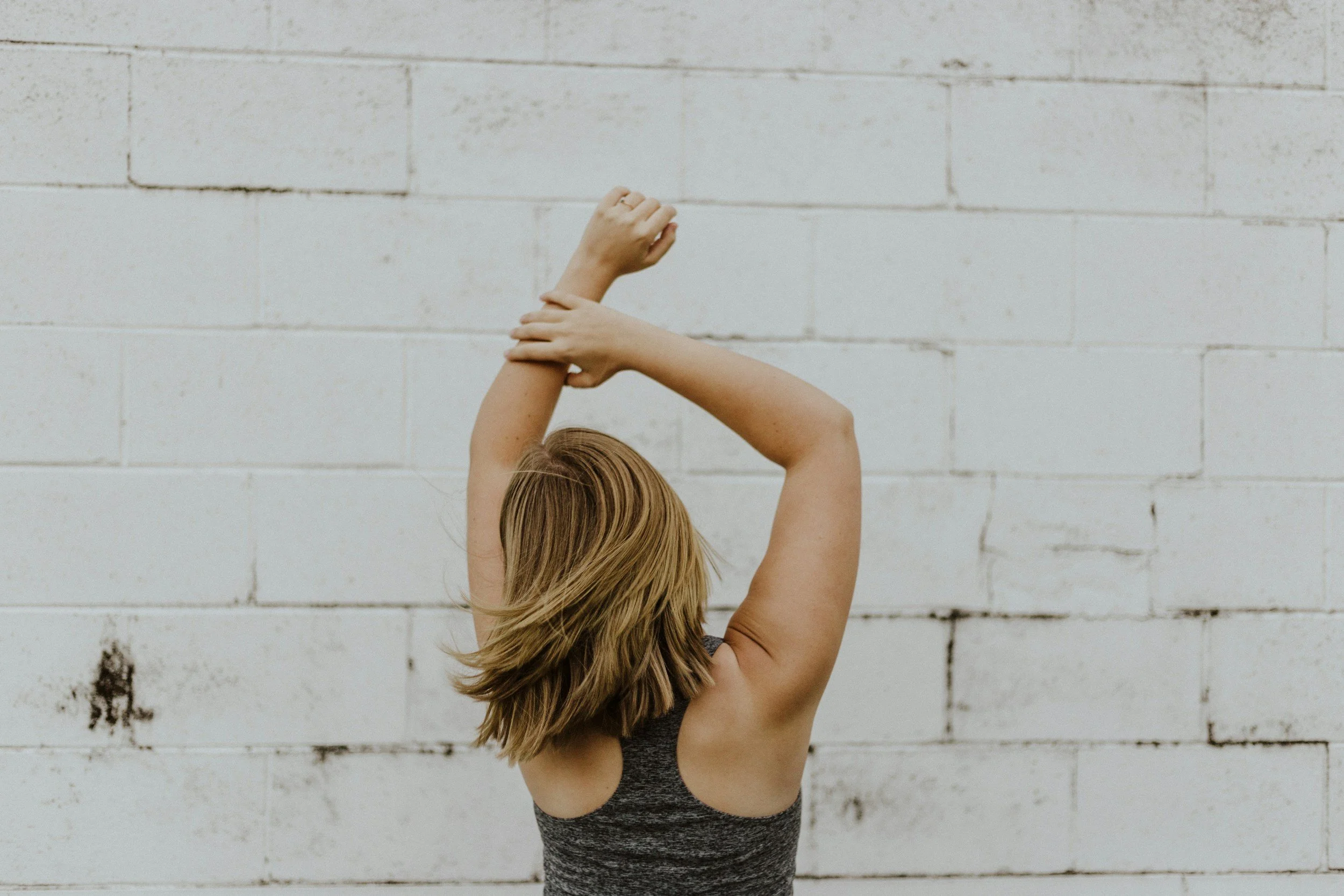 Person standing with their back to the camera and stretching both arms overhead.