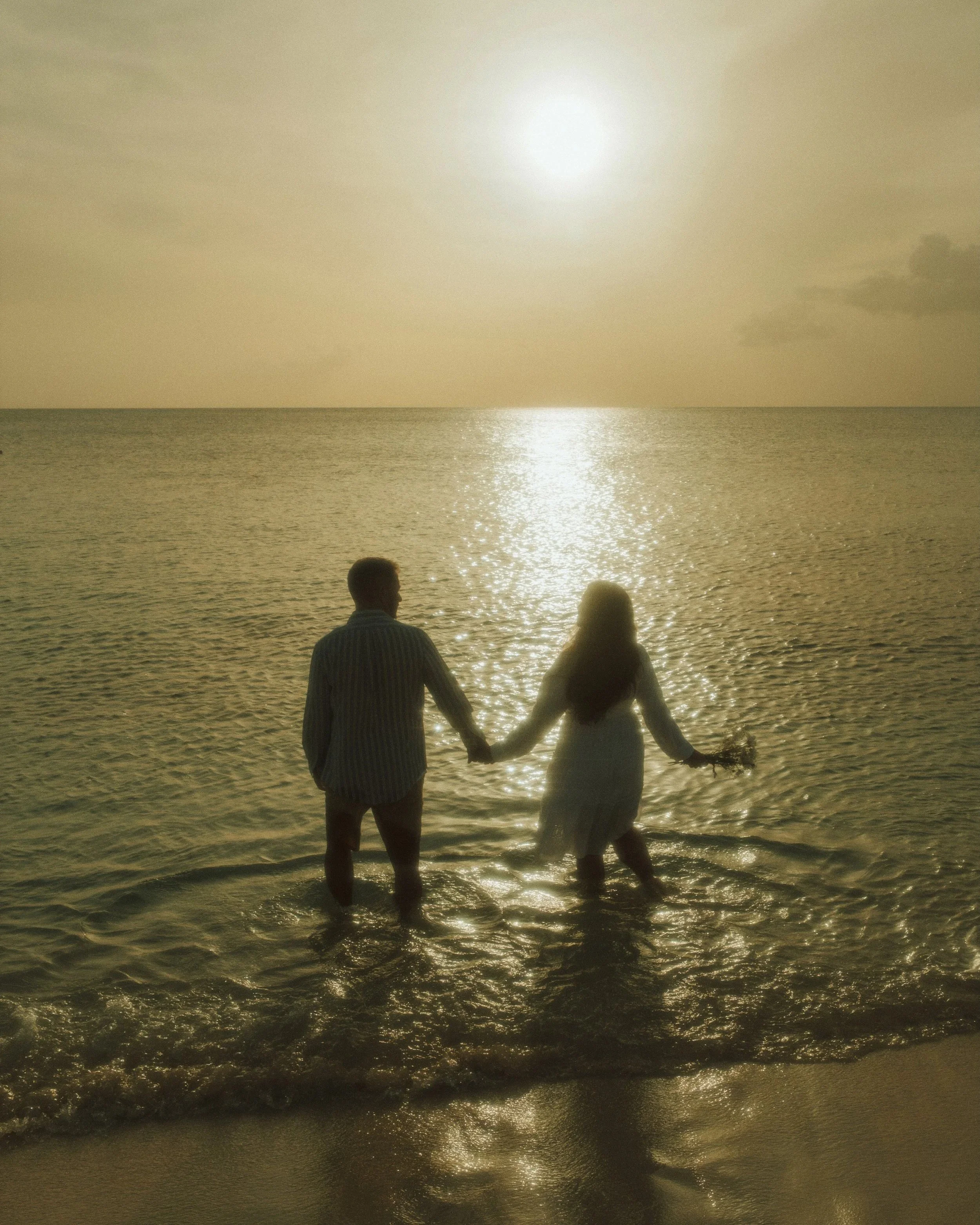 Photo of a couple looking at the golden sunset and ocean glitter captured by Emmedelmar in Cozumel.
