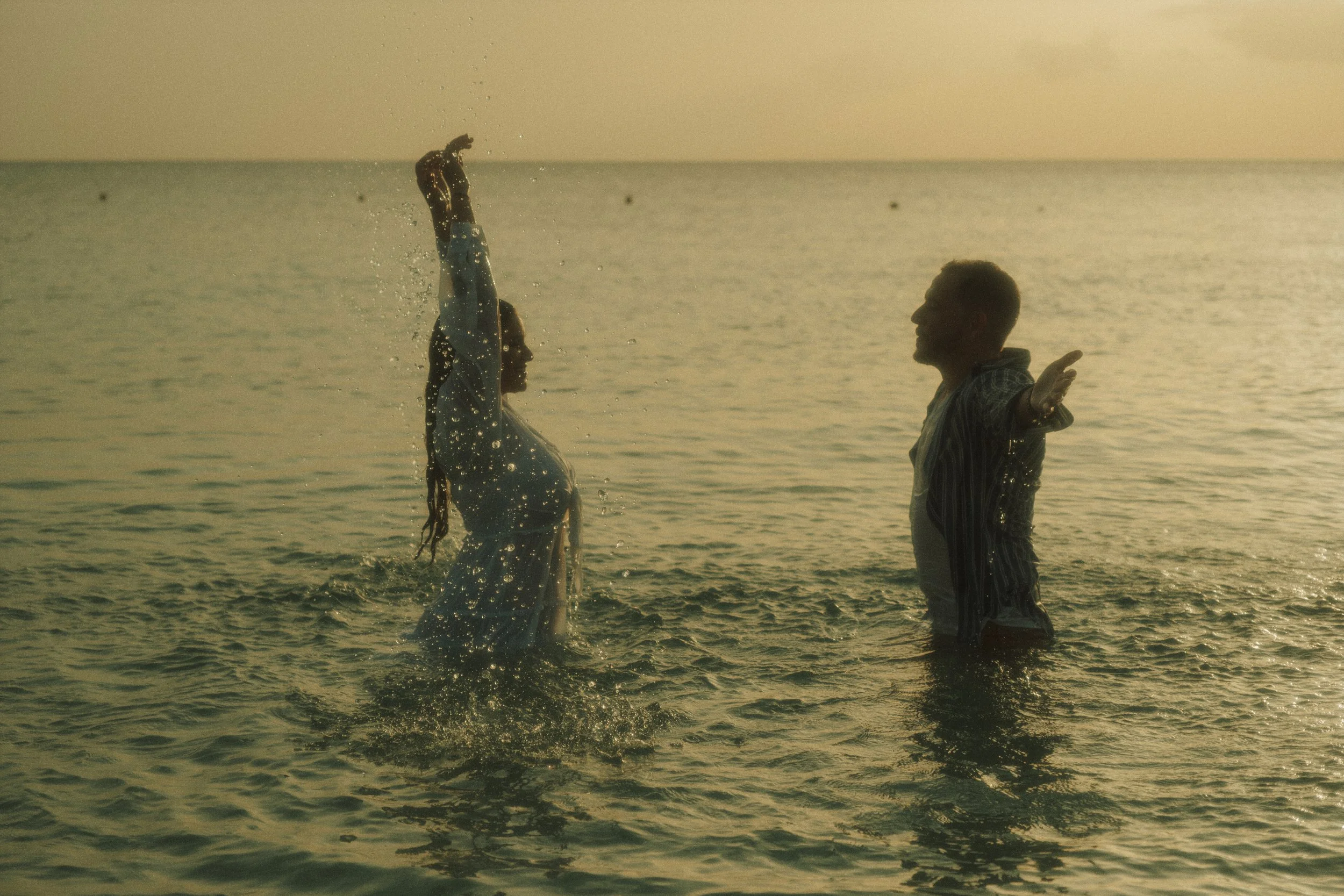 photo of a couple splashing water in the ocean, with a golden sunset in the background captured by Emmedelmar in Cozumel.