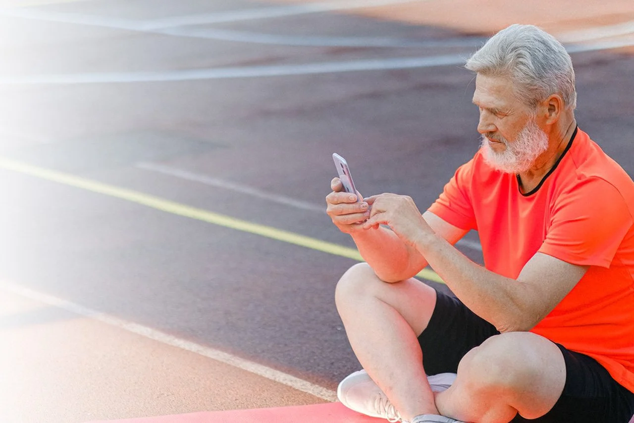 Elderly man in athletic gear using a smartphone outdoors, promoting Mobrise Health's care plans that encourage patient activity and loyalty to healthcare providers.