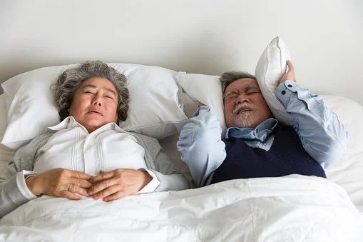 Woman Snoring while Man Covers His Ears with a Pillow