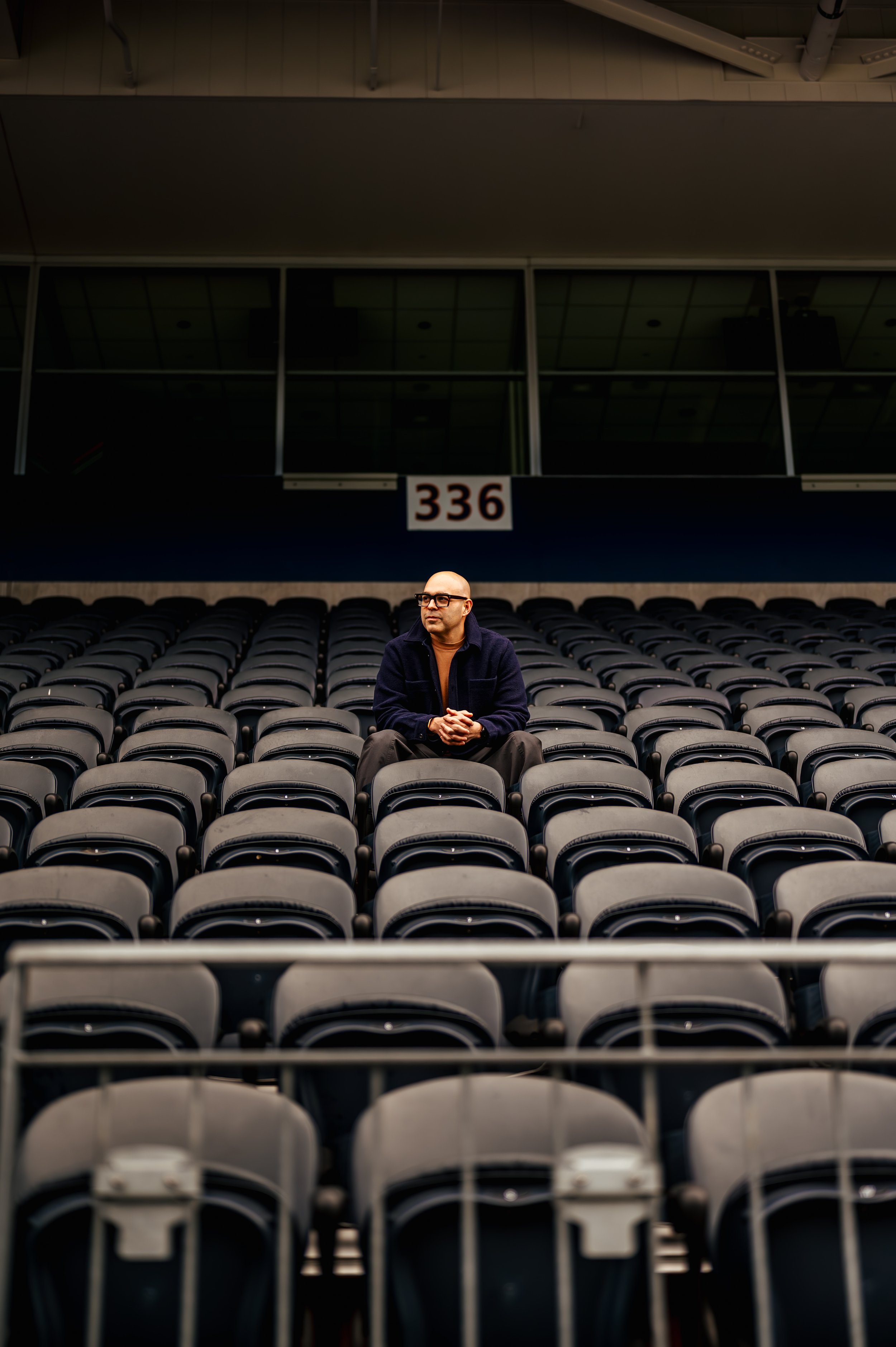 A man sitting alone in a large empty auditorium with rows of black chairs and a balcony with a sign displaying the number 336.