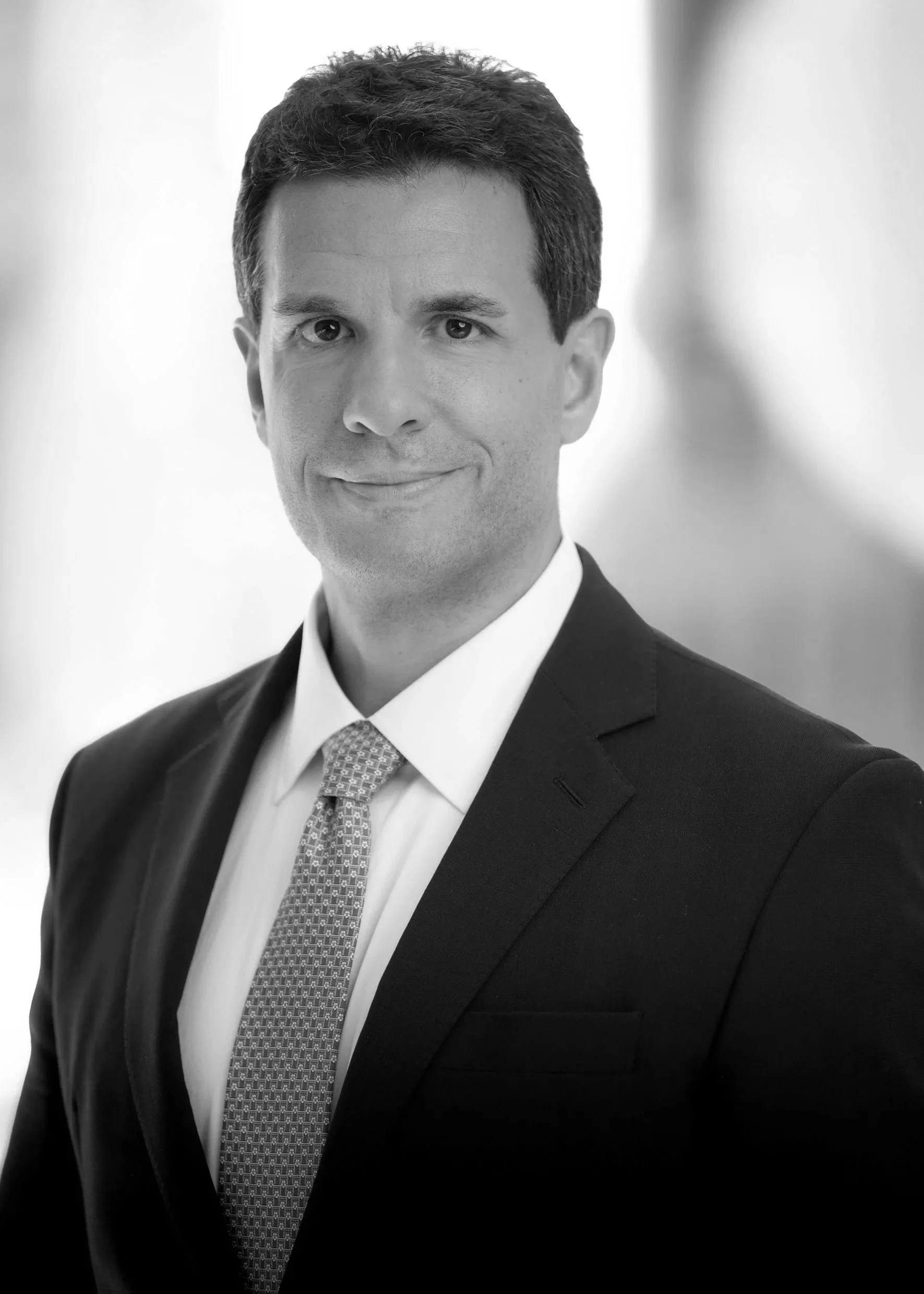 Black and white portrait of a smiling woman with short hair, wearing a suit and jewelry.