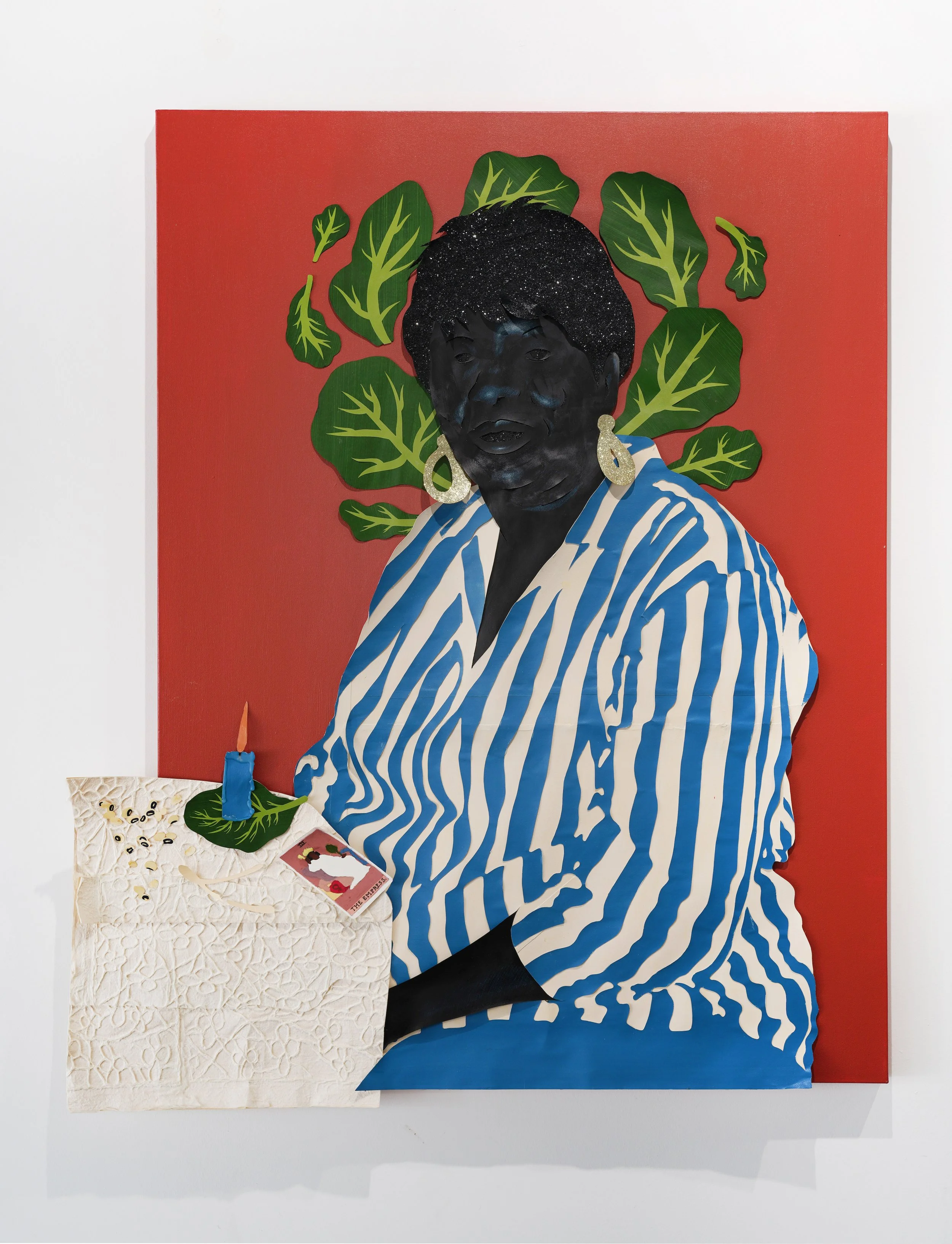 Portrait of a woman sitting behind a table with a white embroidered tablecloth. There is a candle burning on top of a collard green leaf, next to a scattered pile of black eyed peas, a wish bone, and an Empress tarot card.